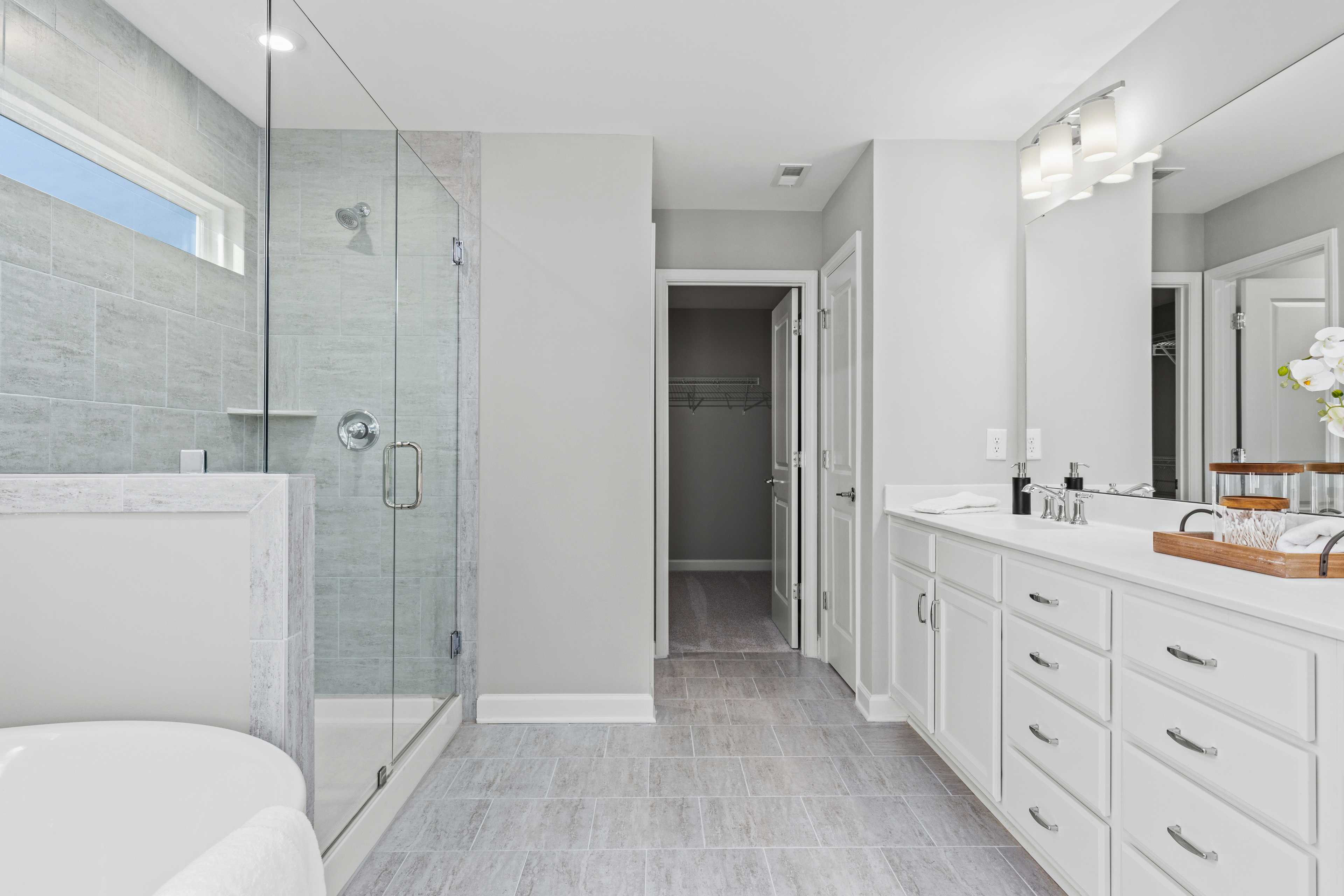 Modern bathroom at Enclave at Belmont in Belmont NC featuring glass shower white vanity freestanding tub and gray tile