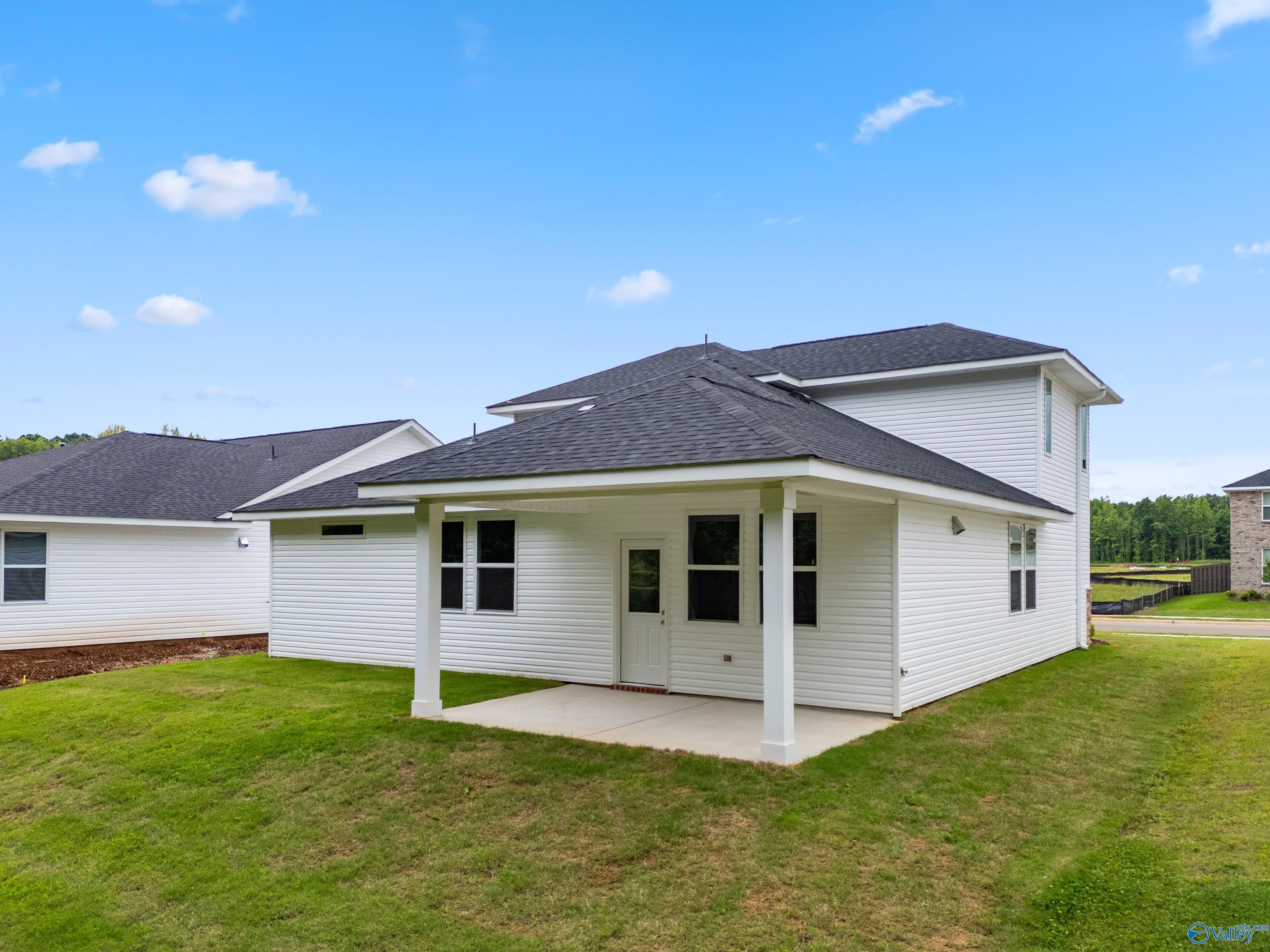 Two-story white Davidson Homes The Stella with covered entry porch, black shingle roof, and lush green yard in Hazel Green, Alabama