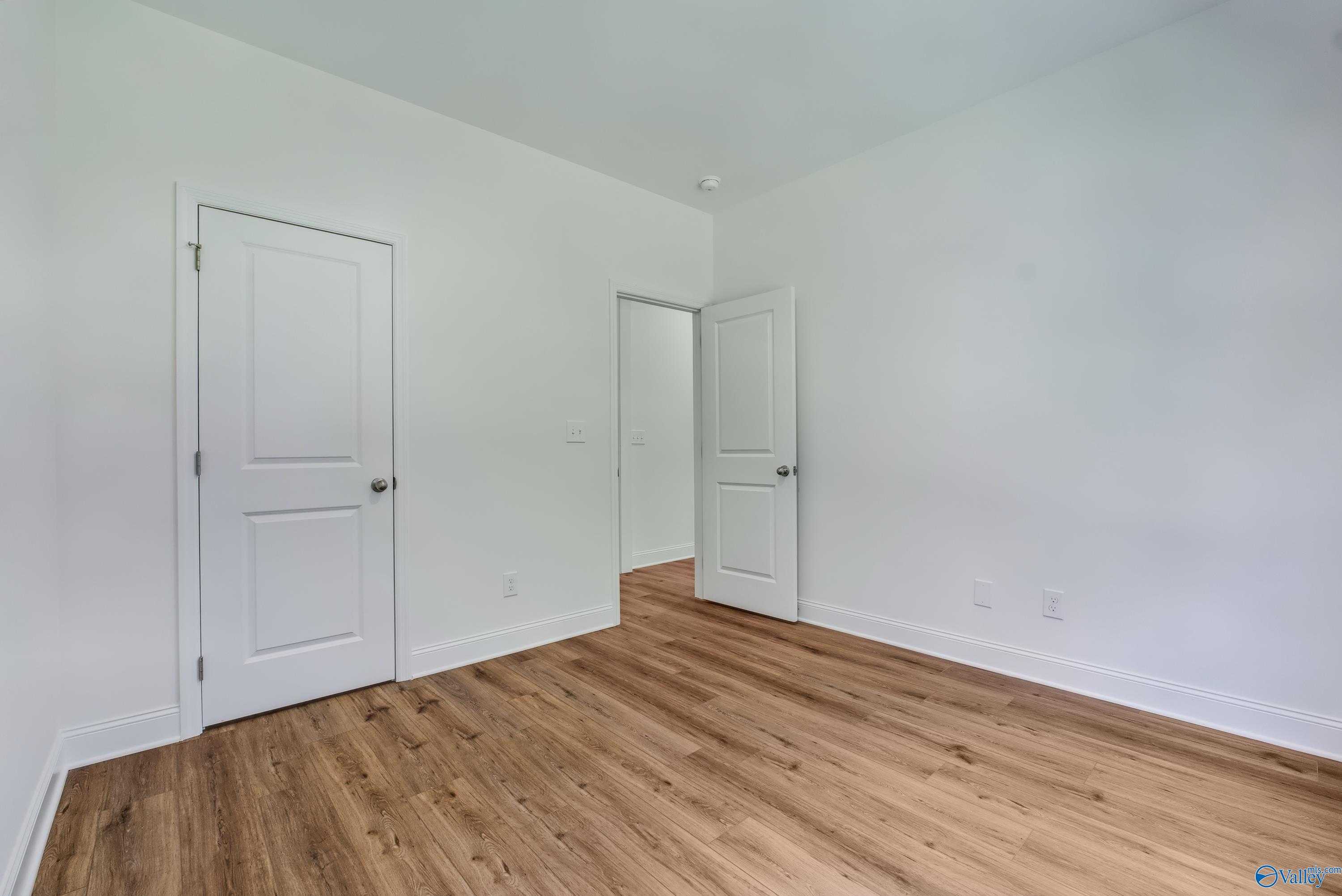Empty bedroom with white walls, light wood floors, and double doors to closet and bath in The Shelby A, Arab, Alabama