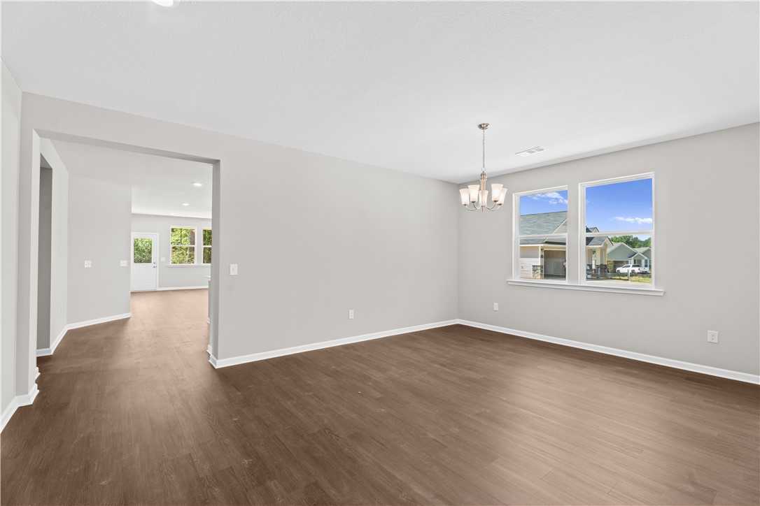Bright living room with hardwood floors, neutral walls, chandelier, and large windows in Evermore Homes The Orion, Cusseta, Alabama