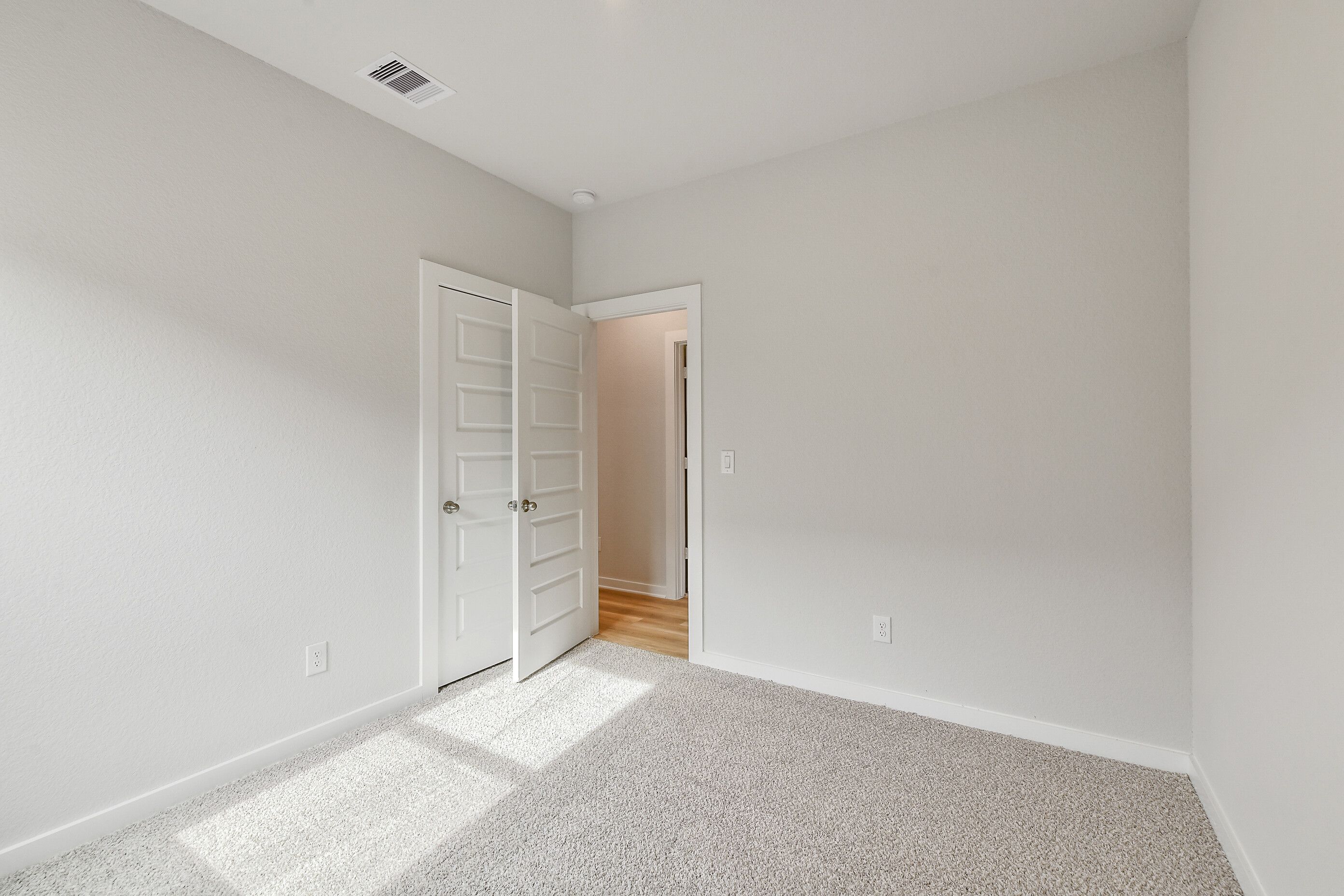 Spacious bedroom with light gray walls, beige carpet, open double closet doors, and natural light in Davidson Homes The Colorado G, Magnolia, Texas