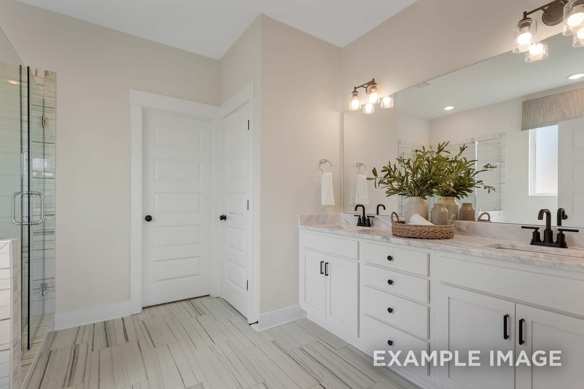 Elegant primary bathroom with double vanity, white shaker cabinets, glass shower, and greenery in Davidson Homes The Ridgeport C, Gallatin, TN