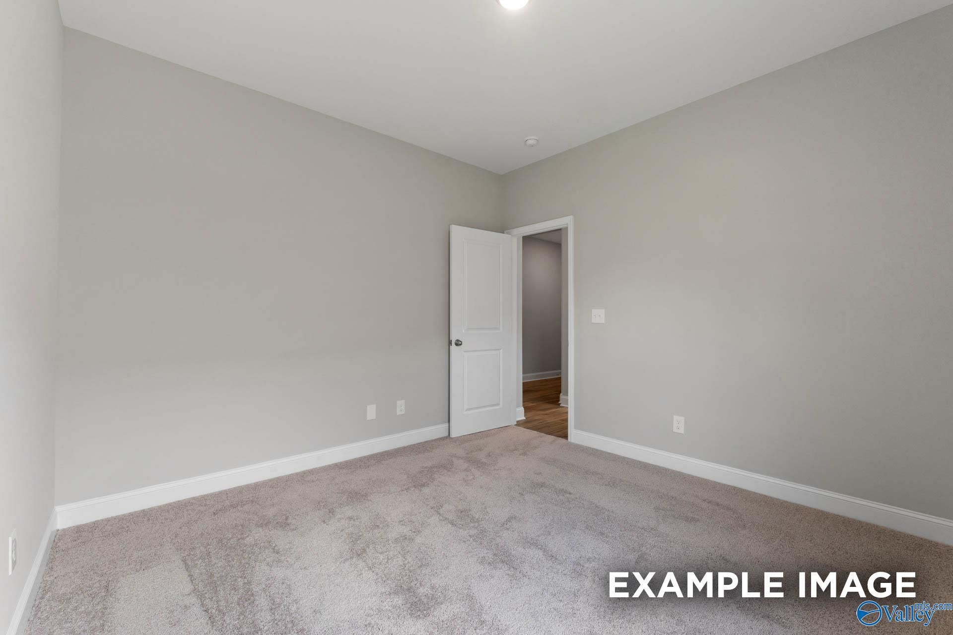 Spacious empty bedroom with neutral gray walls, carpet flooring, and open door in Davidson Homes The Everett, Meridianville, Alabama
