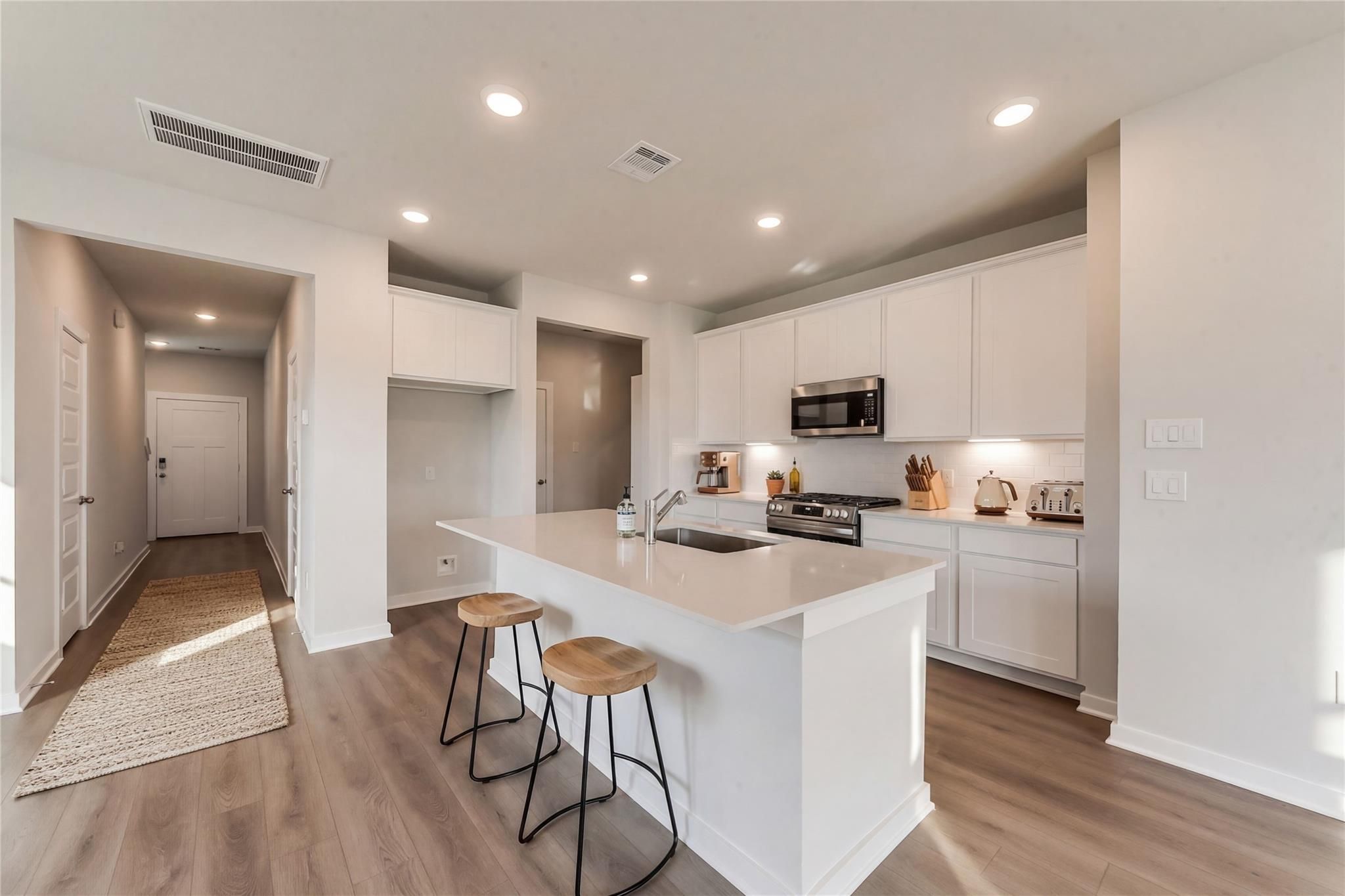 Modern white kitchen with quartz island, stainless appliances, and bar stools in Davidson Homes Brazos E, Dayton Texas