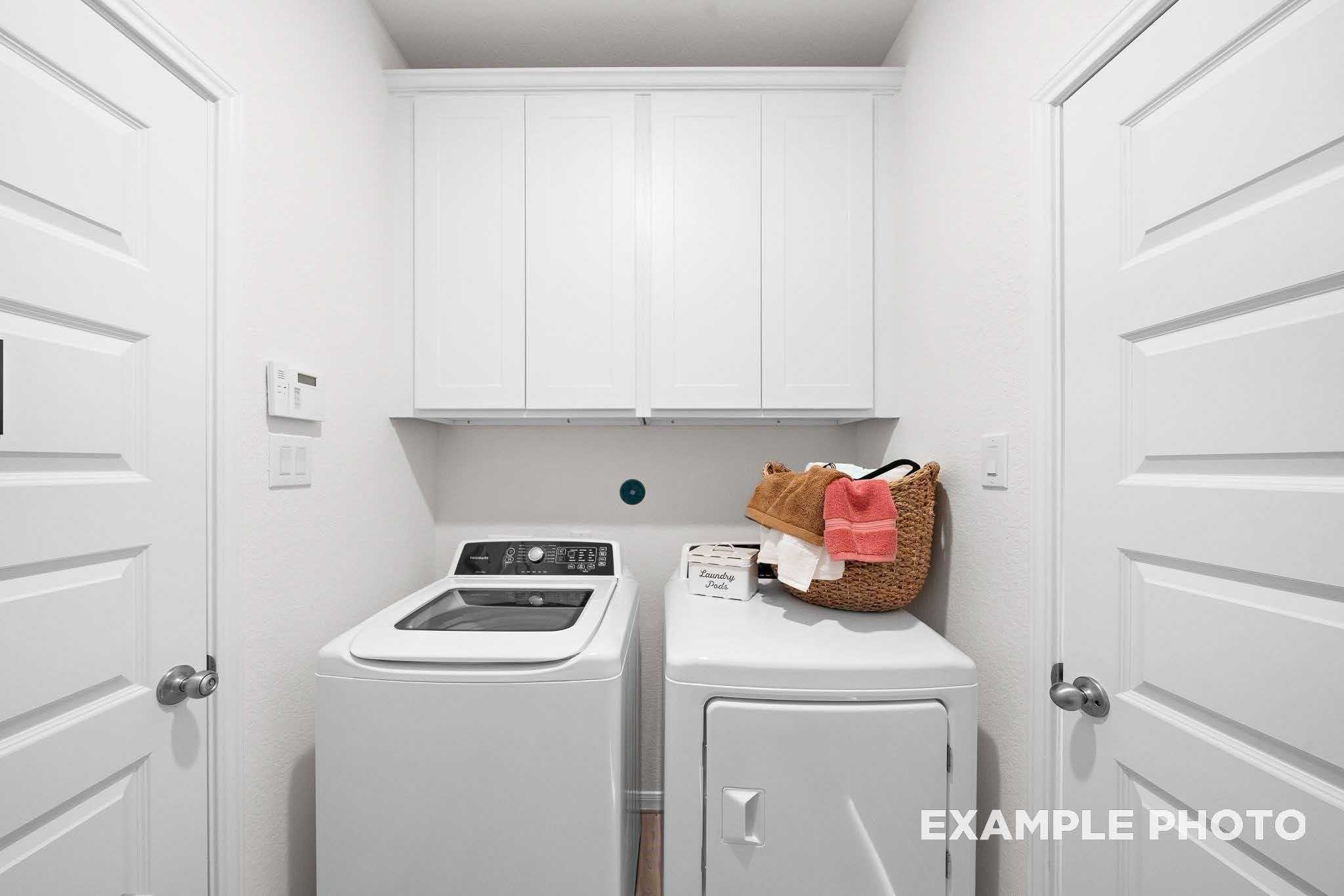 Spacious laundry room with white cabinets, front-load washer, dryer, and storage shelf in Davidson Homes The Sabine F, Magnolia, Texas