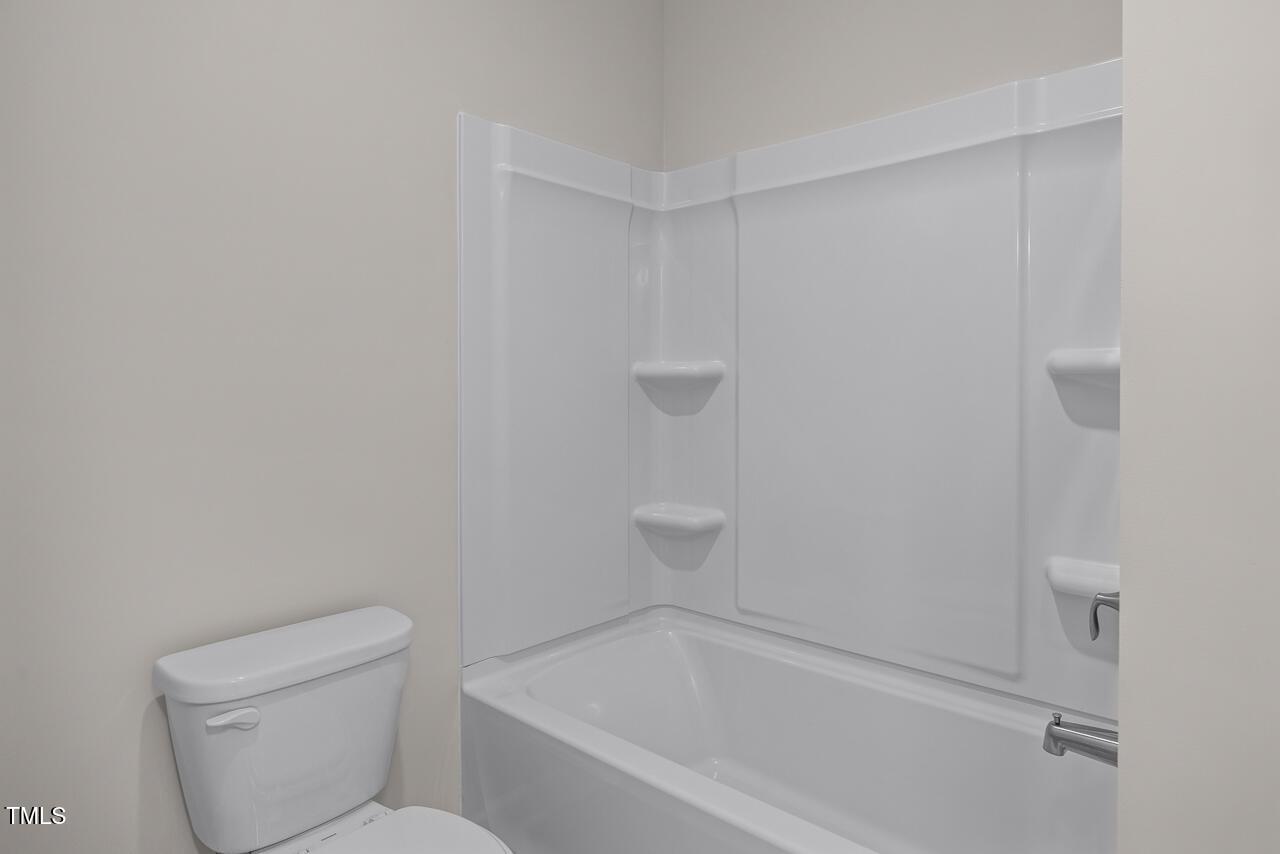 Modern bathroom with white tub-shower combo, toilet, and corner shelves in Davidson Homes The Aspen B, Wake Forest, NC