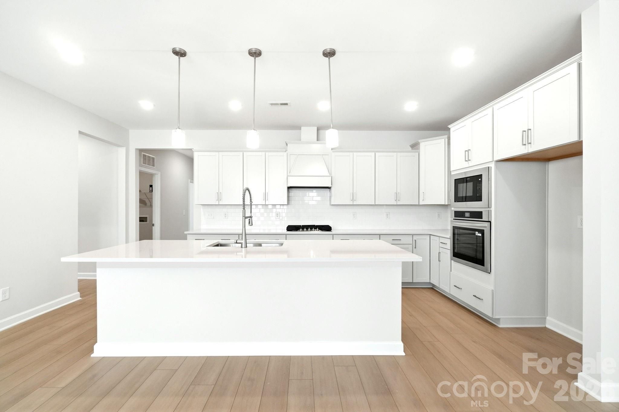 Modern all-white kitchen with large island and stainless appliances in The Magnolia B floor plan, Windgate, Mooresville.