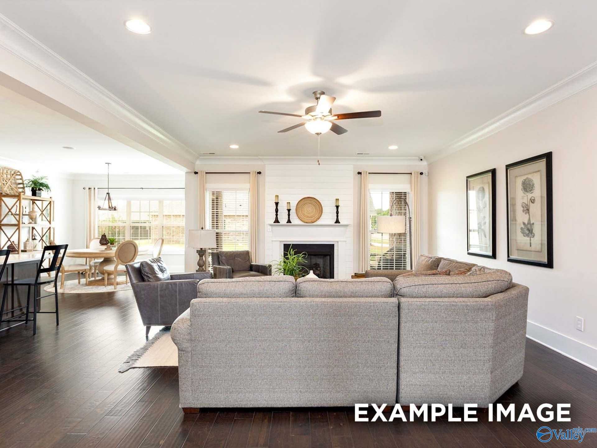 Spacious open great room with gray sectional sofa, stone fireplace, dining area, and hardwood floors in Davidson Homes The Finleigh, Meridianville, Alabama