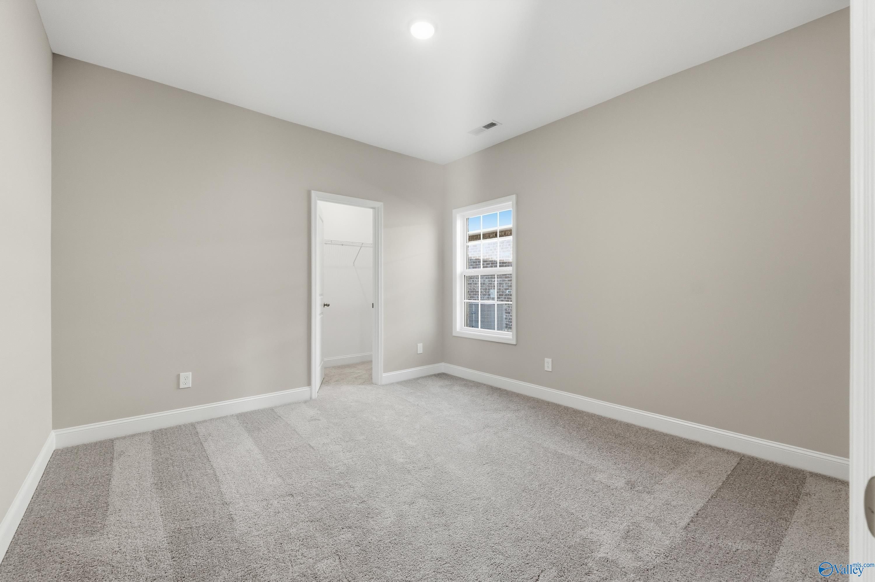 Spacious bedroom with neutral beige walls, gray carpet flooring, large window, and adjacent closet in Davidson Homes The Lanier, Toney, AL