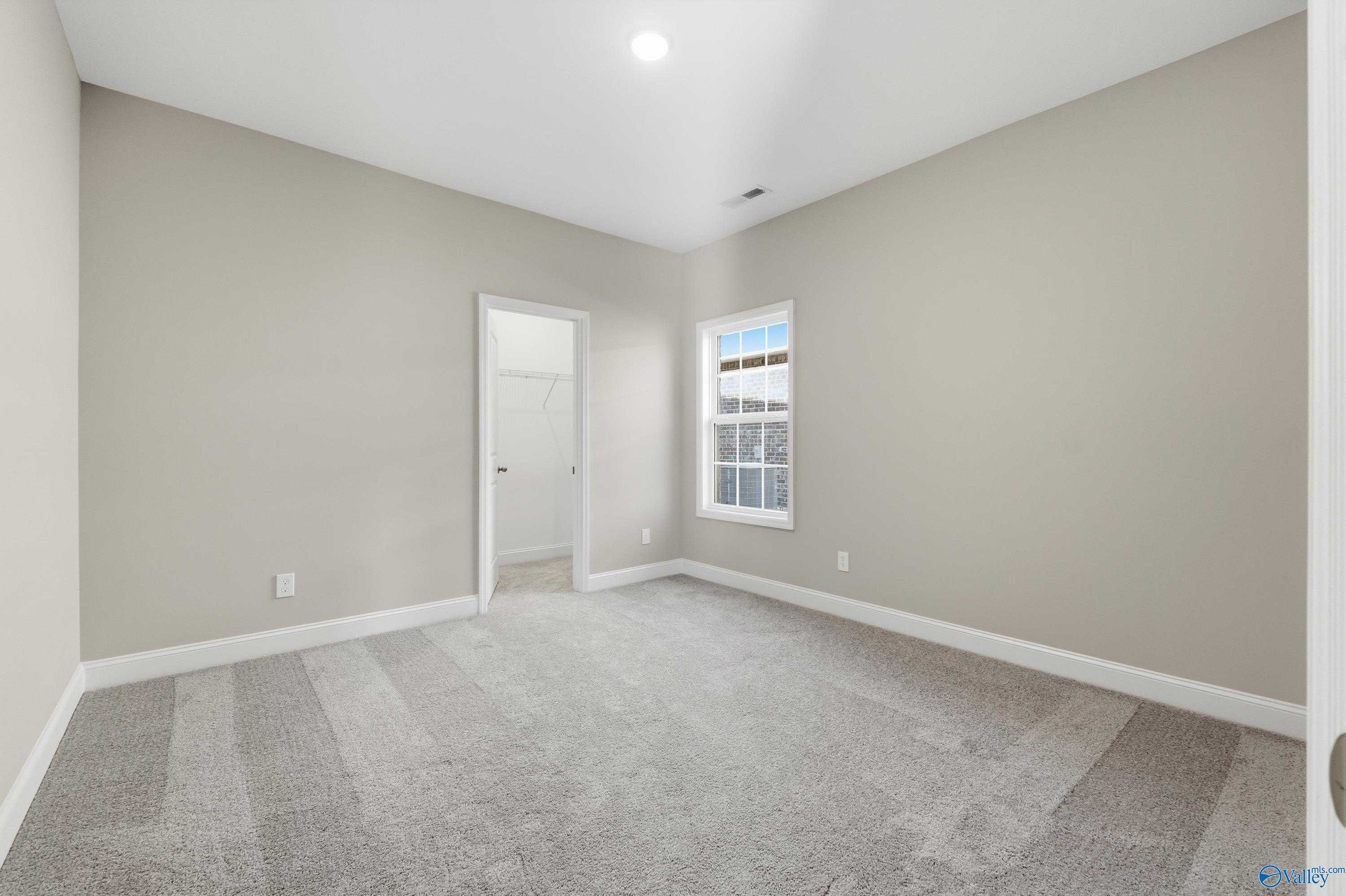 Spacious bedroom with neutral beige walls, gray carpet flooring, large window, and adjacent closet in Davidson Homes The Lanier, Toney, AL