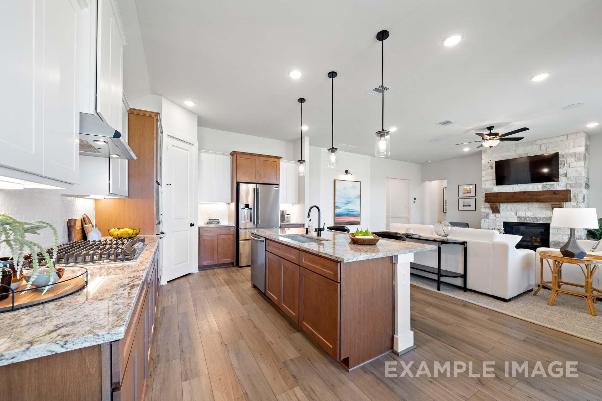 Open-concept kitchen and living room in The Edward C by Davidson Homes featuring granite island, wood cabinets, stainless appliances, stone fireplace