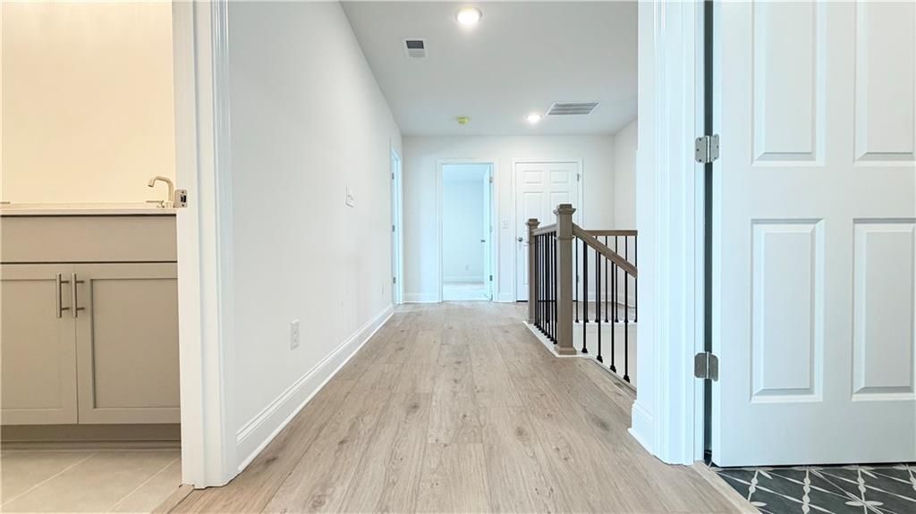Bright upstairs hallway with wood-style flooring and staircase in The Hickory C floor plan by Davidson Homes in Hoschton.