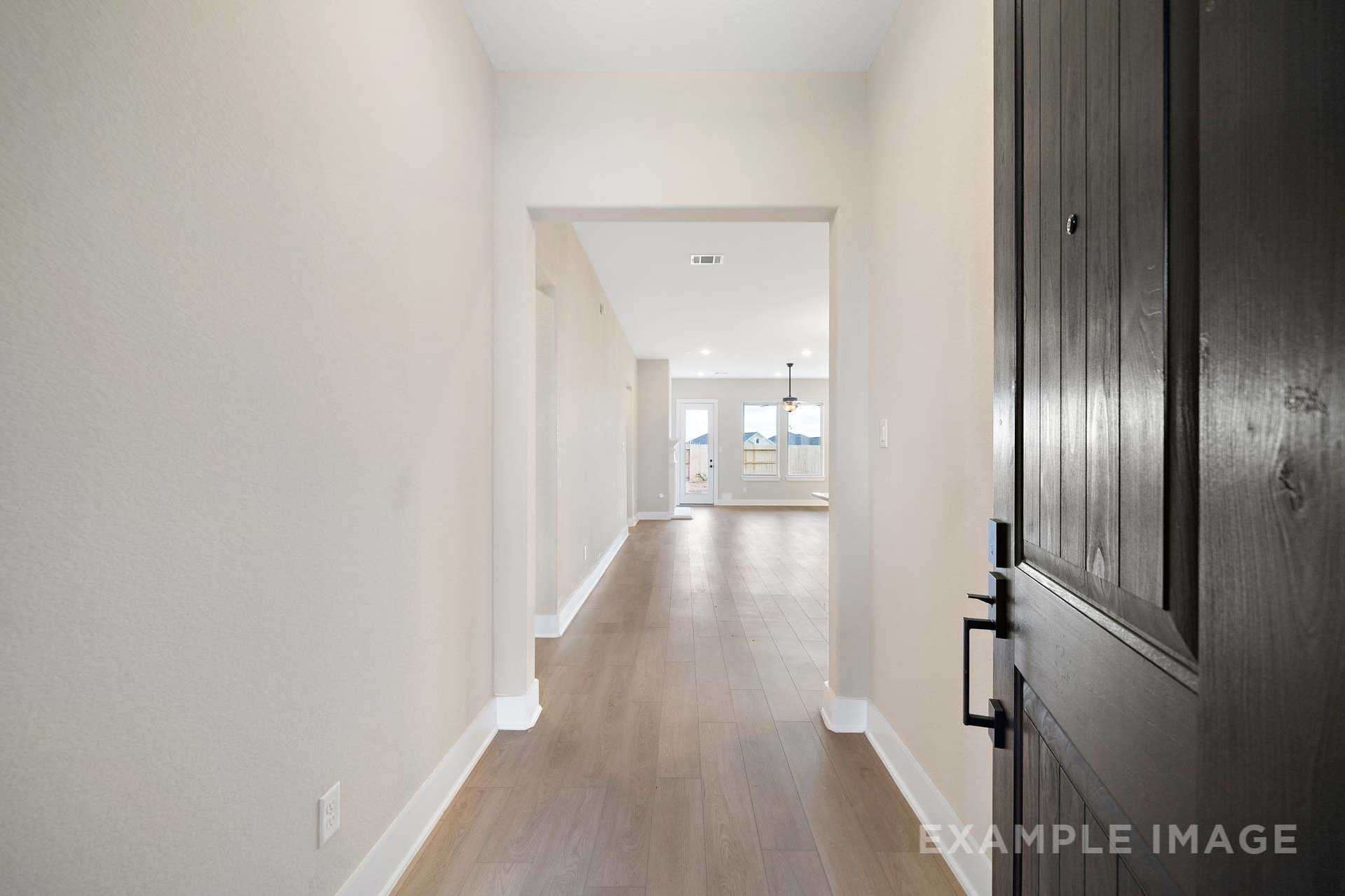 Spacious entryway hallway in The Elizabeth A Davidson Homes design featuring beige walls, hardwood floors, and open archway to sunlit room