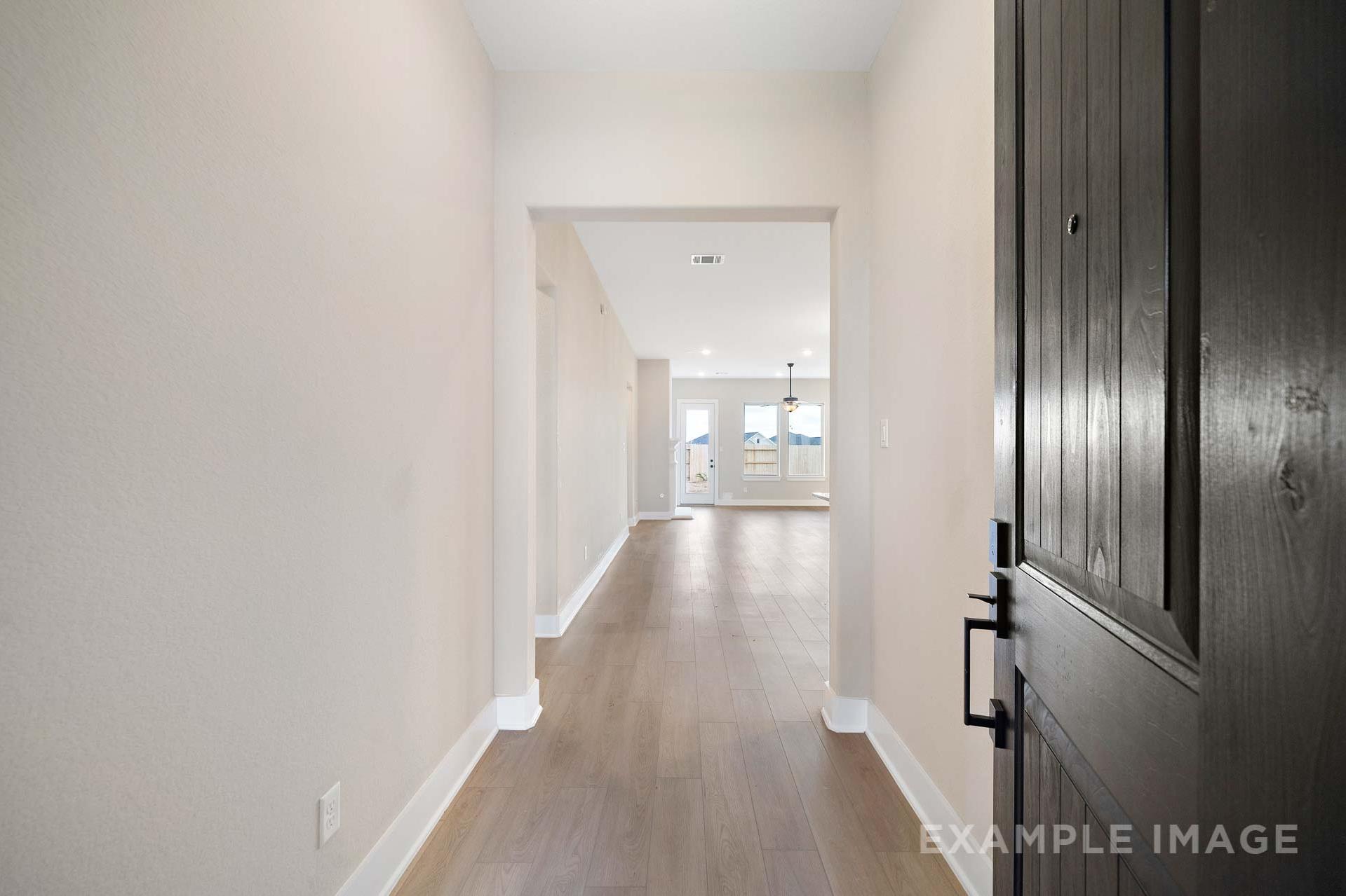 Spacious entryway hallway in The Elizabeth A Davidson Homes design featuring beige walls, hardwood floors, and open archway to sunlit room