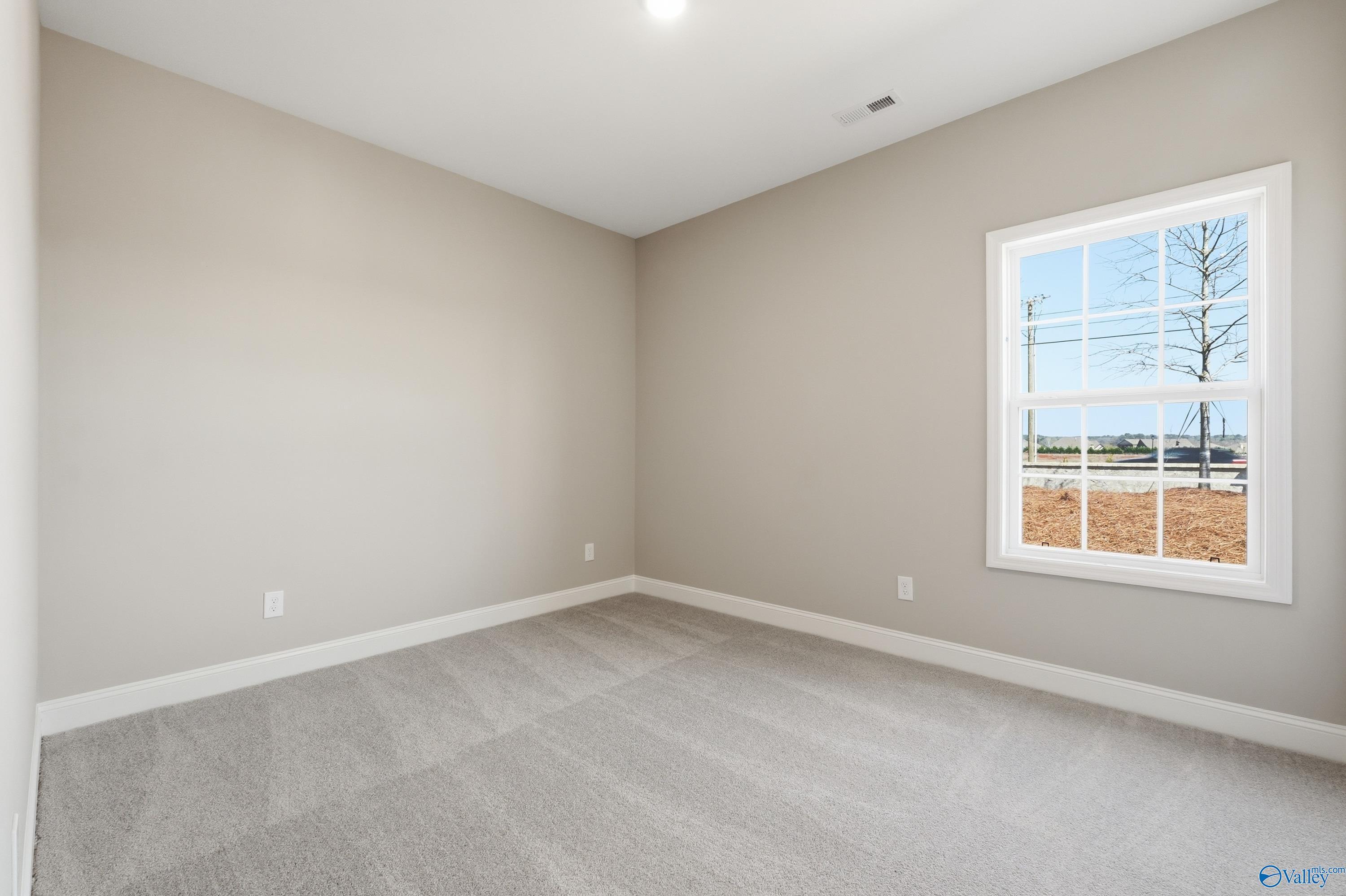 Bright secondary bedroom with beige walls, gray carpet, and large window in Davidson Homes The Rockford, Harvest, Alabama