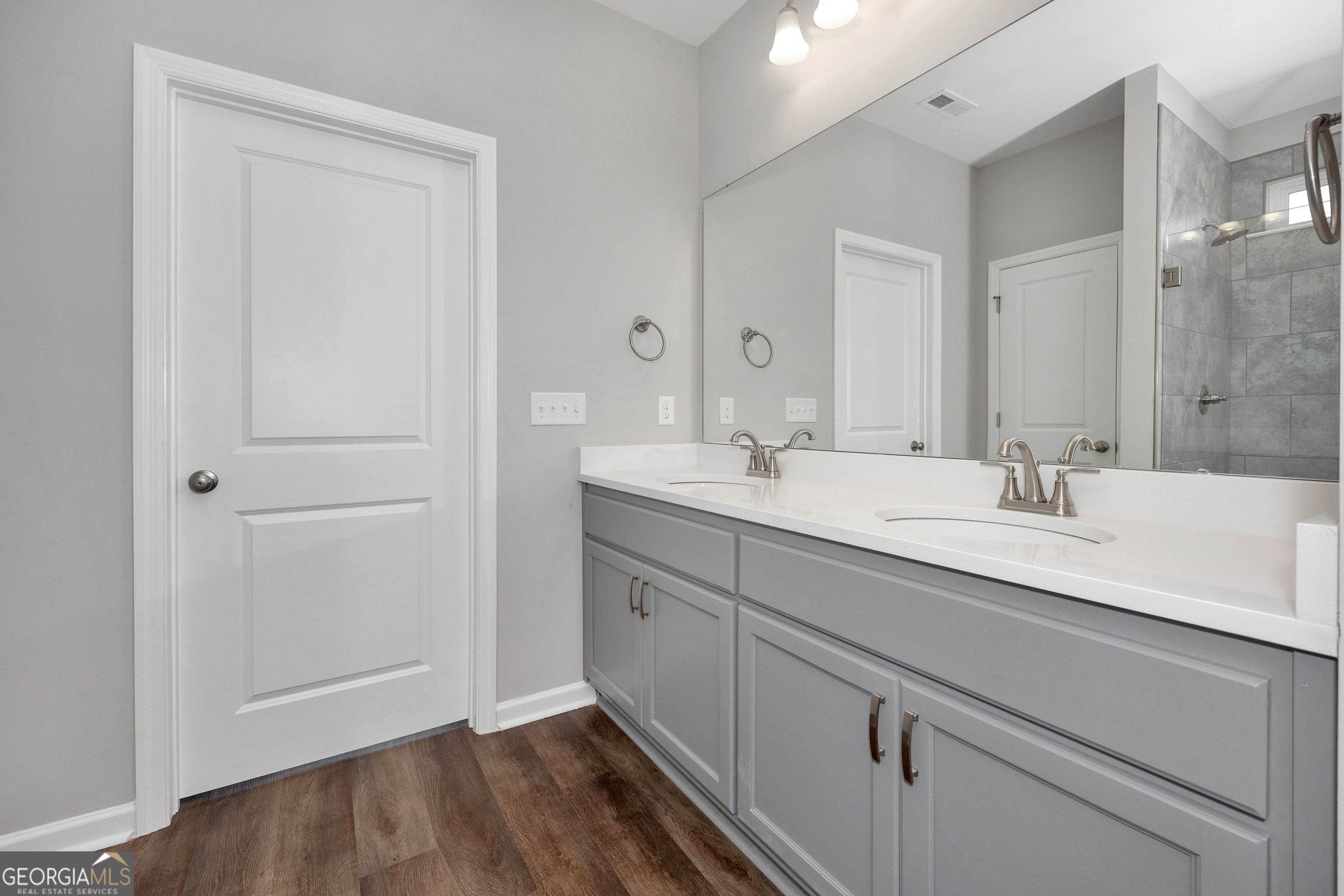 Modern master bathroom featuring double vanity with gray cabinets, white quartz counters, and glass shower in The Luna 4-bedroom home by Evermore Homes in Perry, Georgia