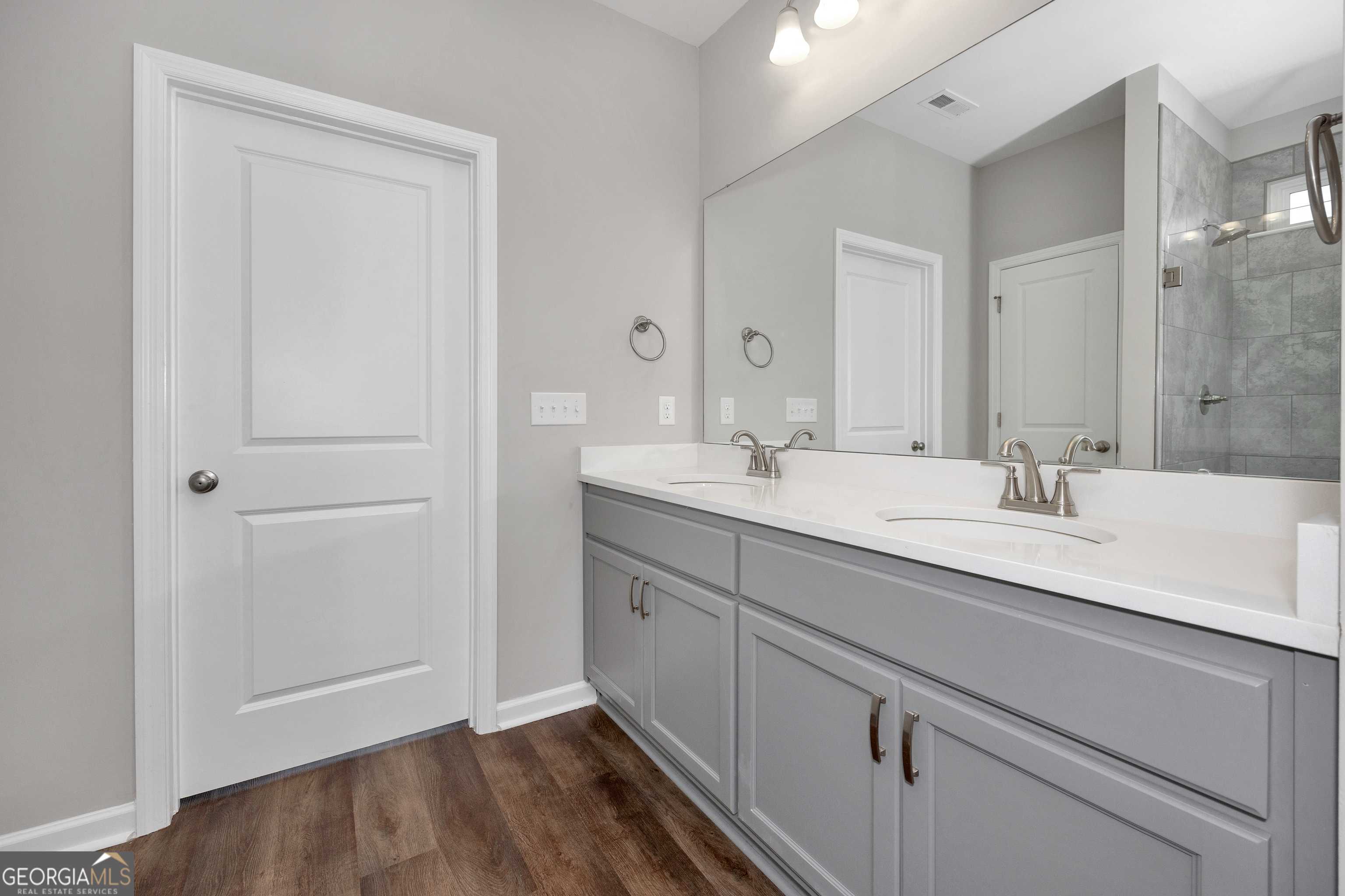 Modern master bathroom featuring double vanity with gray cabinets, white quartz counters, and glass shower in Evermore Homes The Luna, Perry, GA