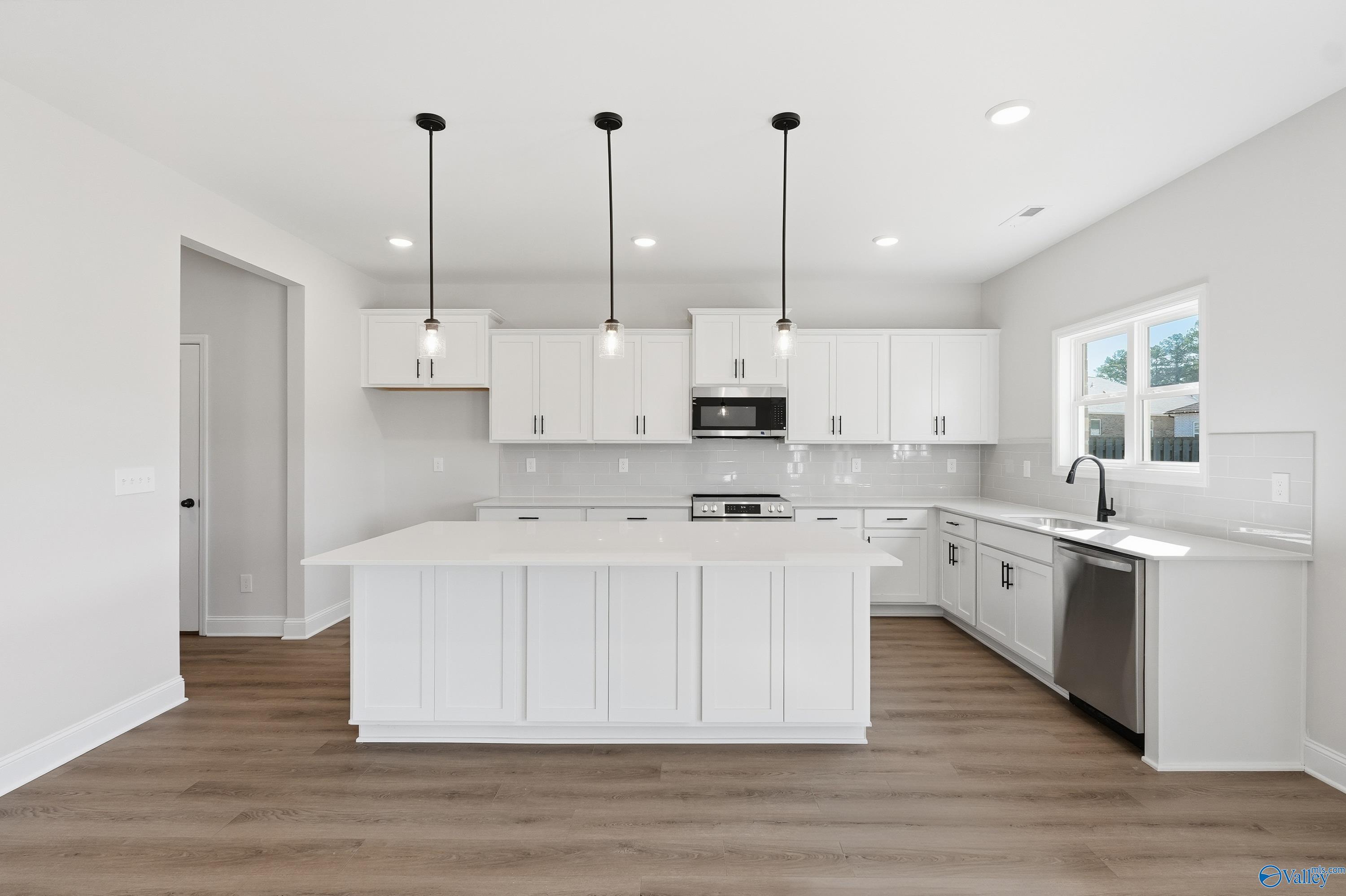 Modern white kitchen island with stainless steel appliances and pendant lights in The Chelsea C by Davidson Homes, Harvest, Alabama