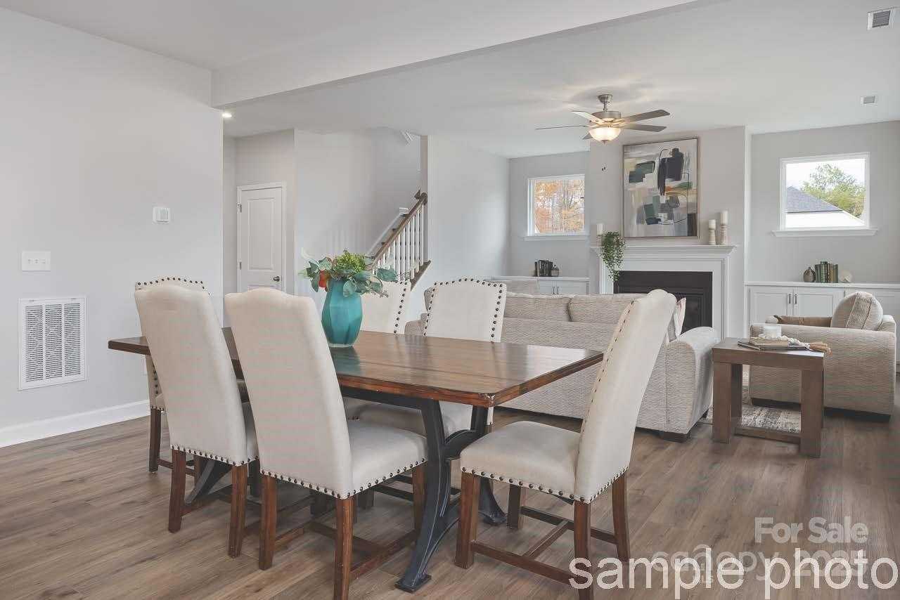 Open dining-living area with wooden table, upholstered chairs, sectional sofa, and fireplace in Davidson Homes The Chestnut F, Belmont, NC