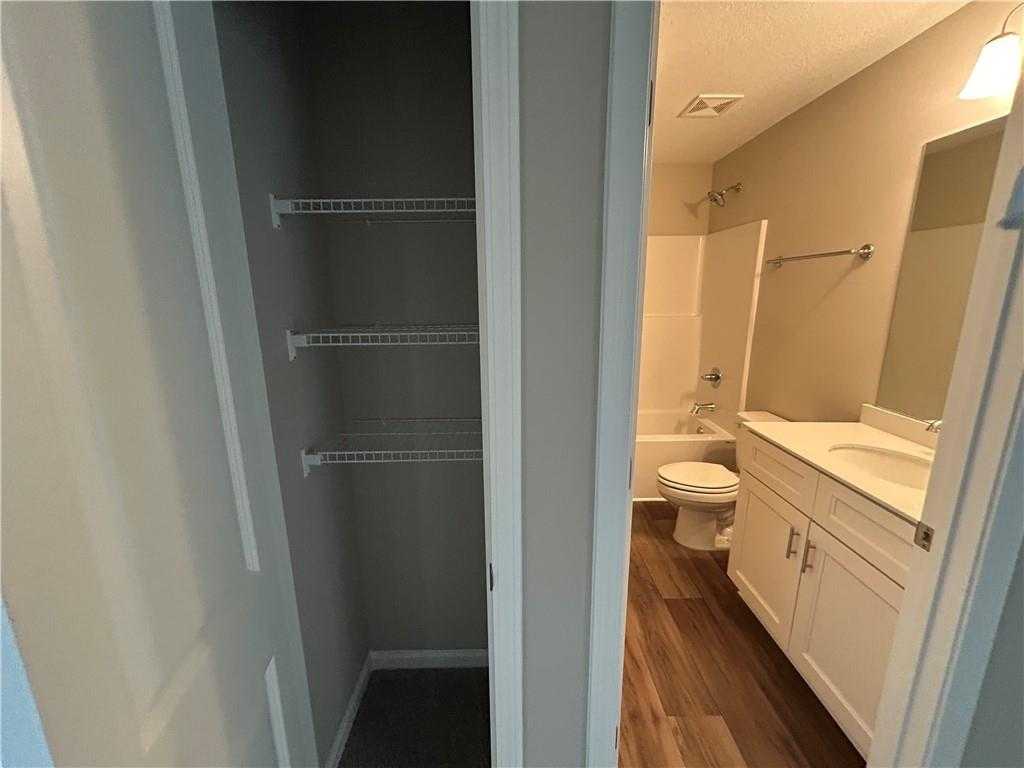 Bright bathroom with tub-shower combo, white vanity sink, toilet, and adjacent open linen closet shelves in Davidson Homes The Washington, Phenix City, AL
