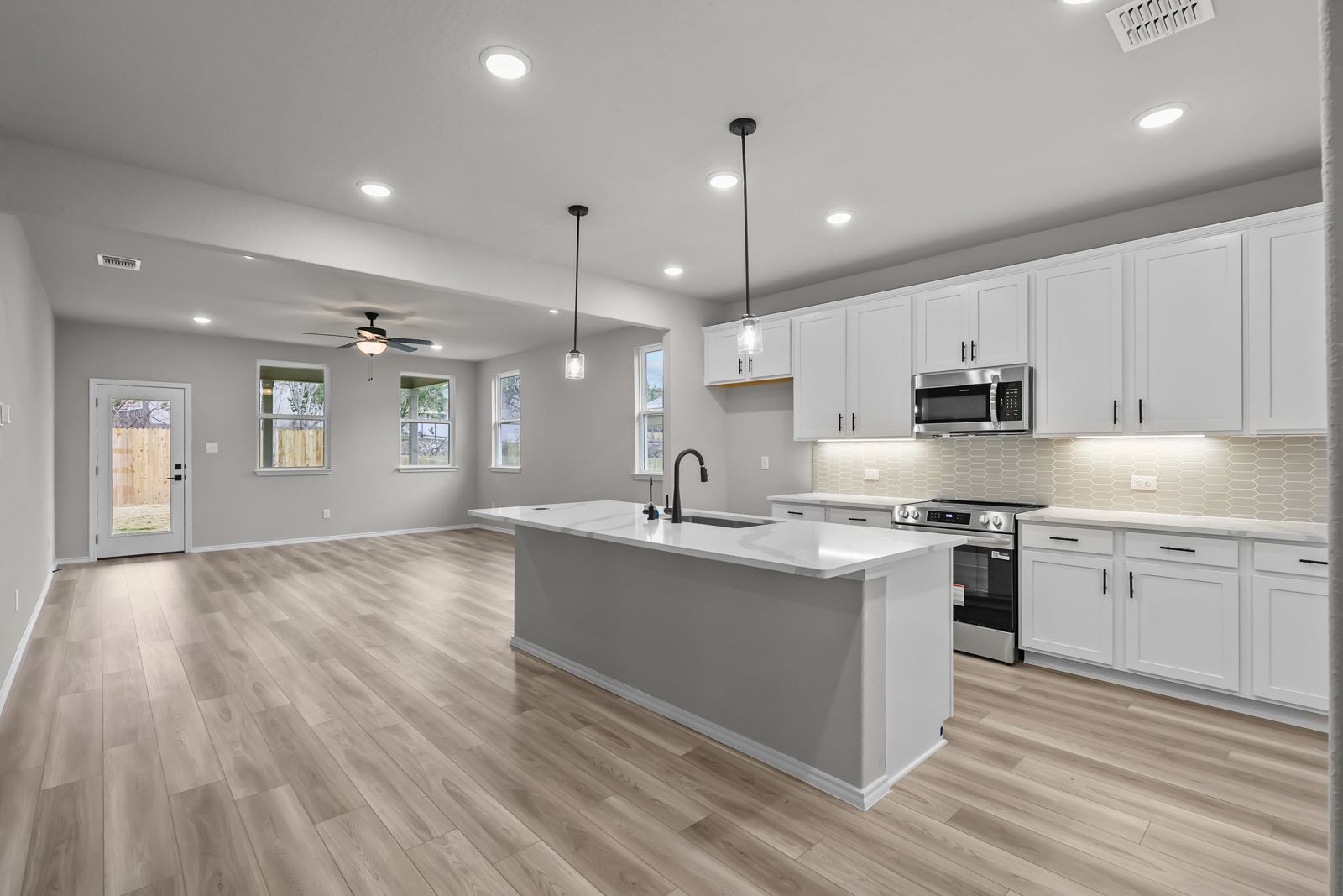 Open-concept kitchen and living area in The Glenwood featuring a large island, white cabinetry, and modern finishes.