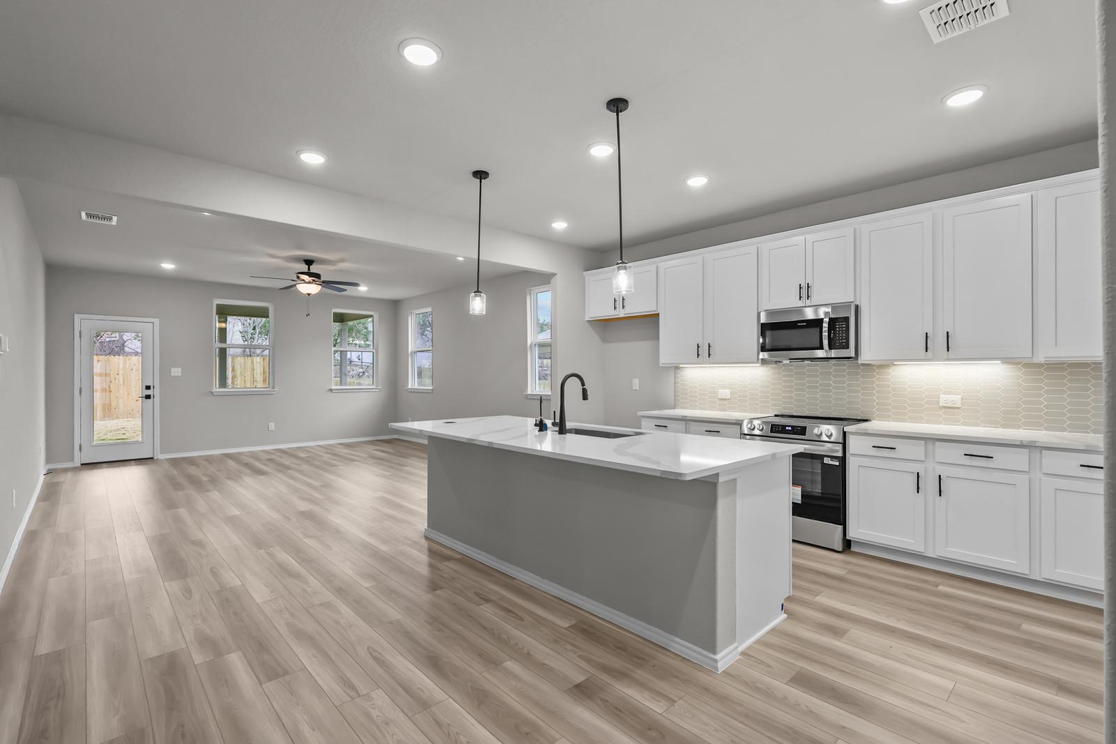 Open-concept kitchen and living area in The Glenwood featuring a large island, white cabinetry, and modern finishes.