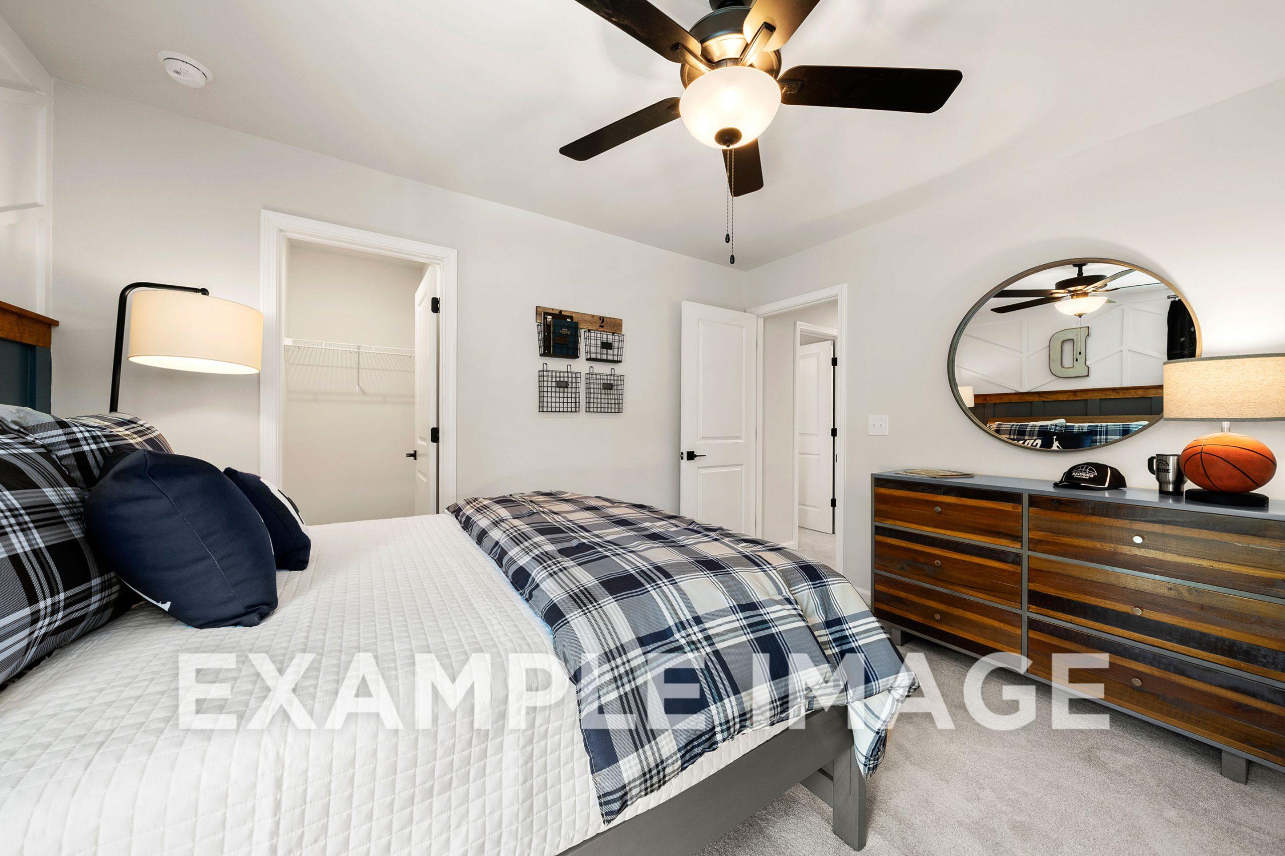 Spacious upper-floor bedroom in The Hickory B featuring plaid bedding, wooden dresser, round mirror, and basketball decor