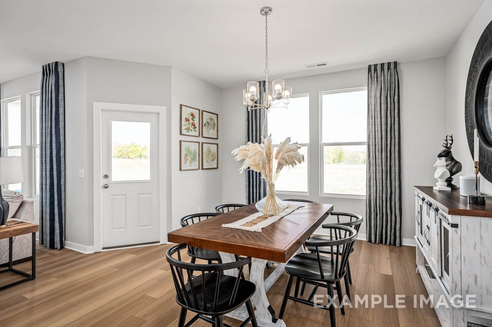 Elegant dining room with farmhouse wooden table, black chairs, chandelier, and large windows in Davidson Homes The Franklin B, White House, TN
