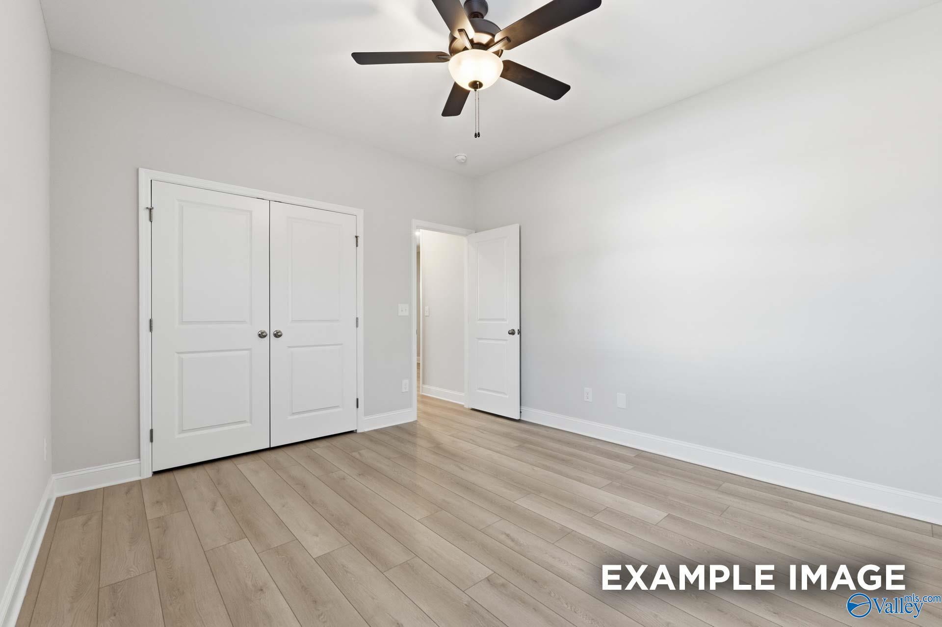 Spacious bedroom with ceiling fan, double white closet doors, open entry, light gray walls, and luxury vinyl plank flooring in Davidson Homes The Harrison C, Madison, Alabama
