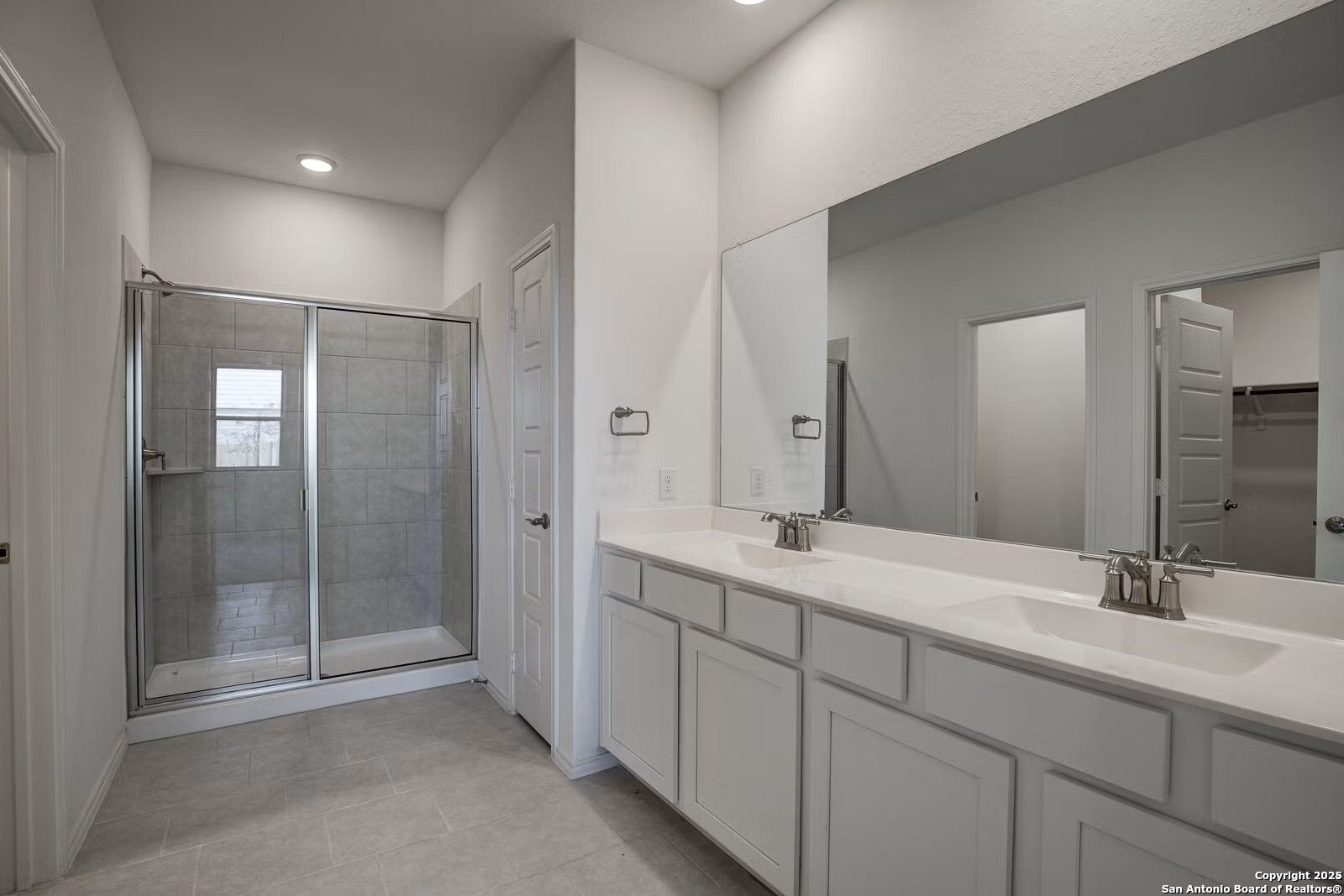 Modern master bathroom featuring double white vanity, large mirror, and glass walk-in shower in Davidson Homes The Douglas B, Seguin, Texas