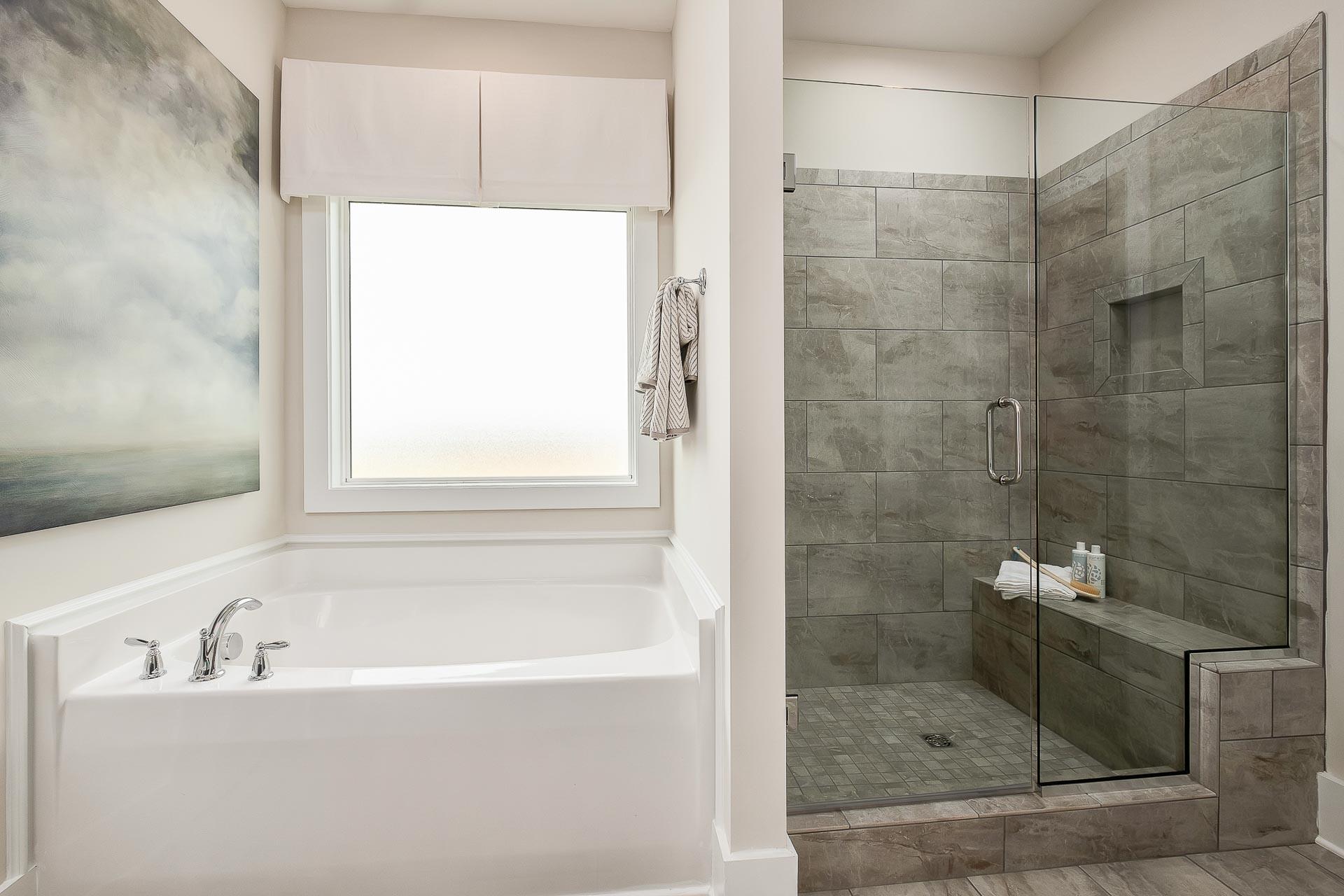 Luxury master bathroom in The Everett featuring freestanding white tub, gray tiled walk-in shower with glass enclosure, and window