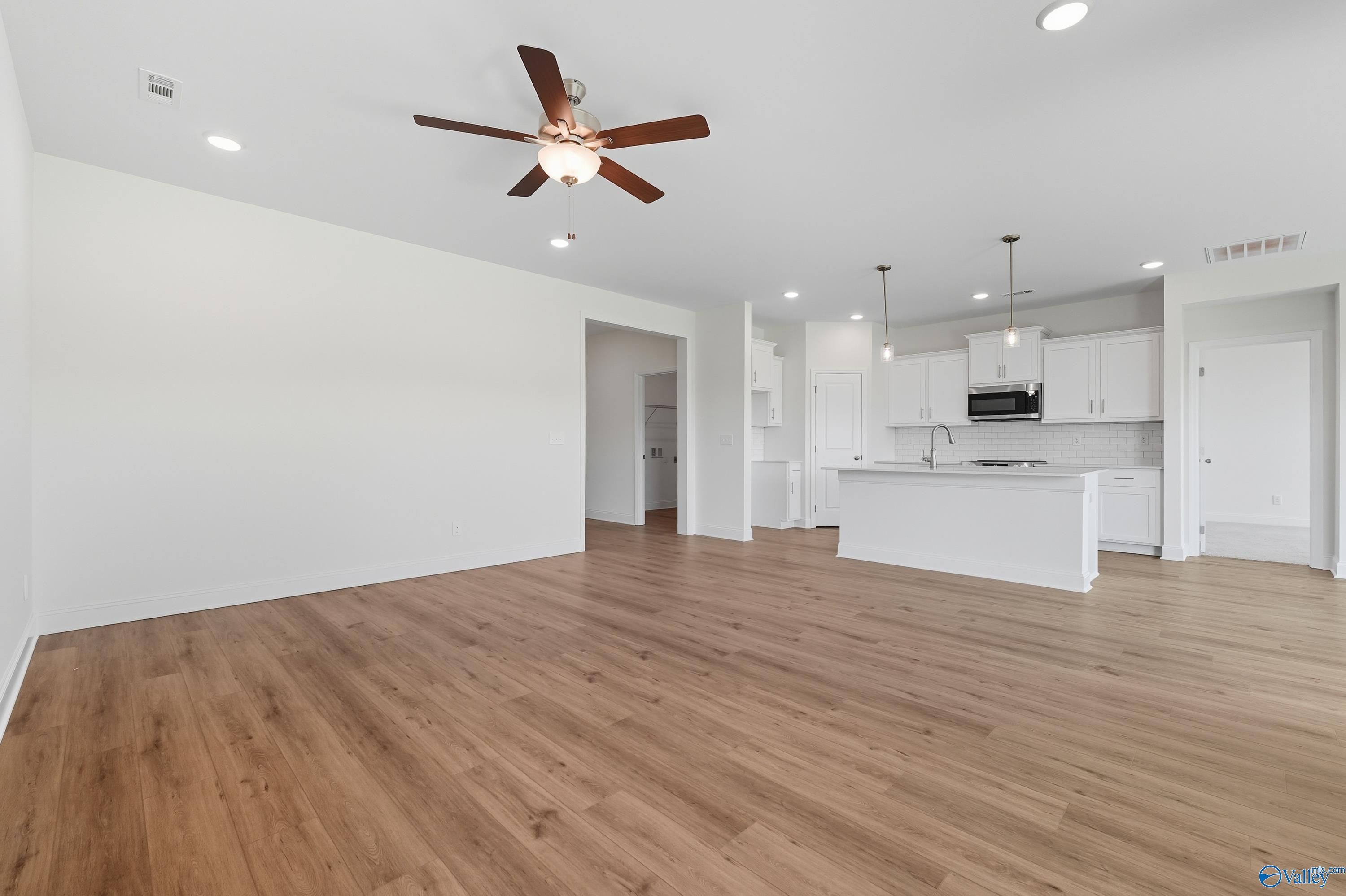 Open-concept kitchen with white cabinets, island sink, and hardwood floors in The Everett 4-bedroom home, Meridianville, Alabama