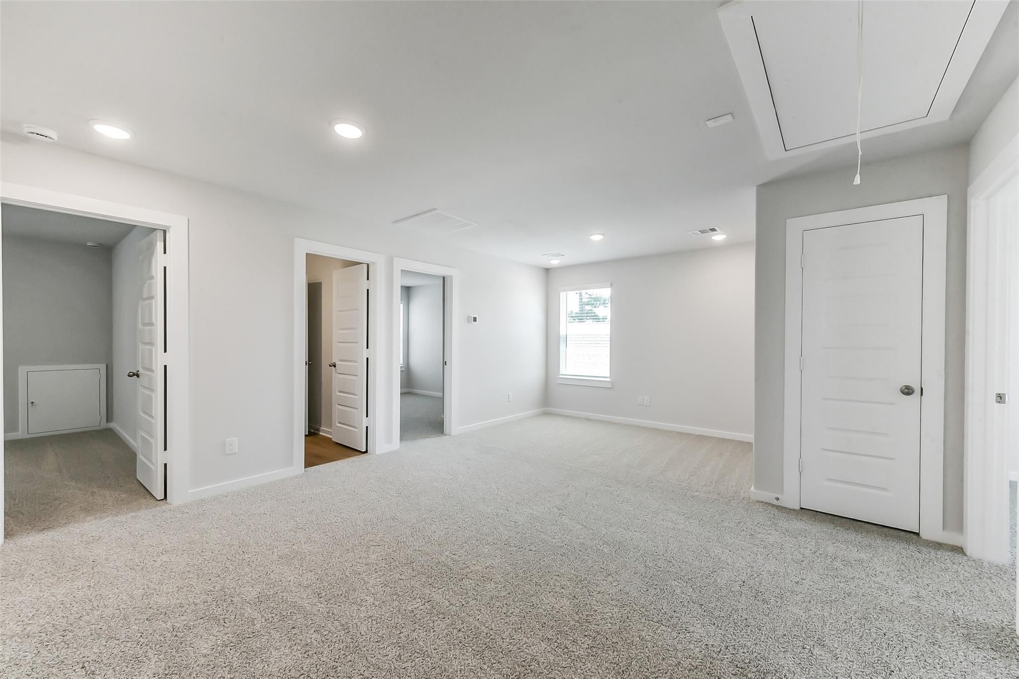 Bright upstairs hallway with multiple open bedroom doors, gray carpet, and recessed lighting in Davidson Homes The Brazos E, Magnolia Texas