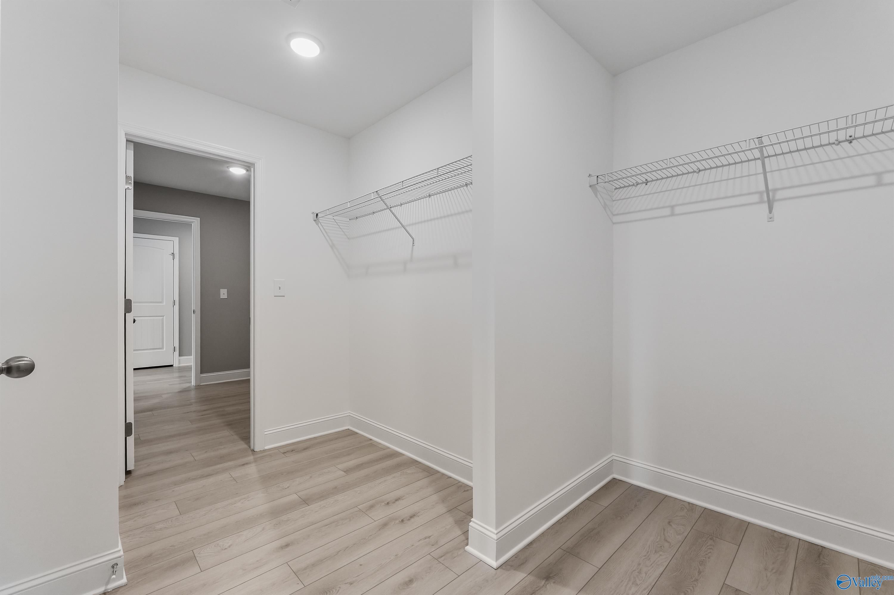 Spacious walk-in closet with wire shelving, white walls, hardwood floors in master suite of Davidson Homes The Everett B, Athens AL
