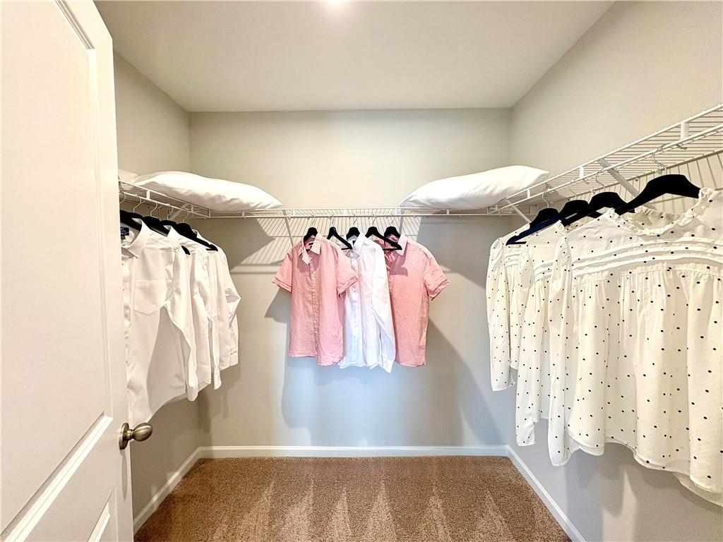 Spacious walk-in closet with white wire shelving, hanging blouses and pillows in Davidson Homes The Monroe A, Emerson, Georgia
