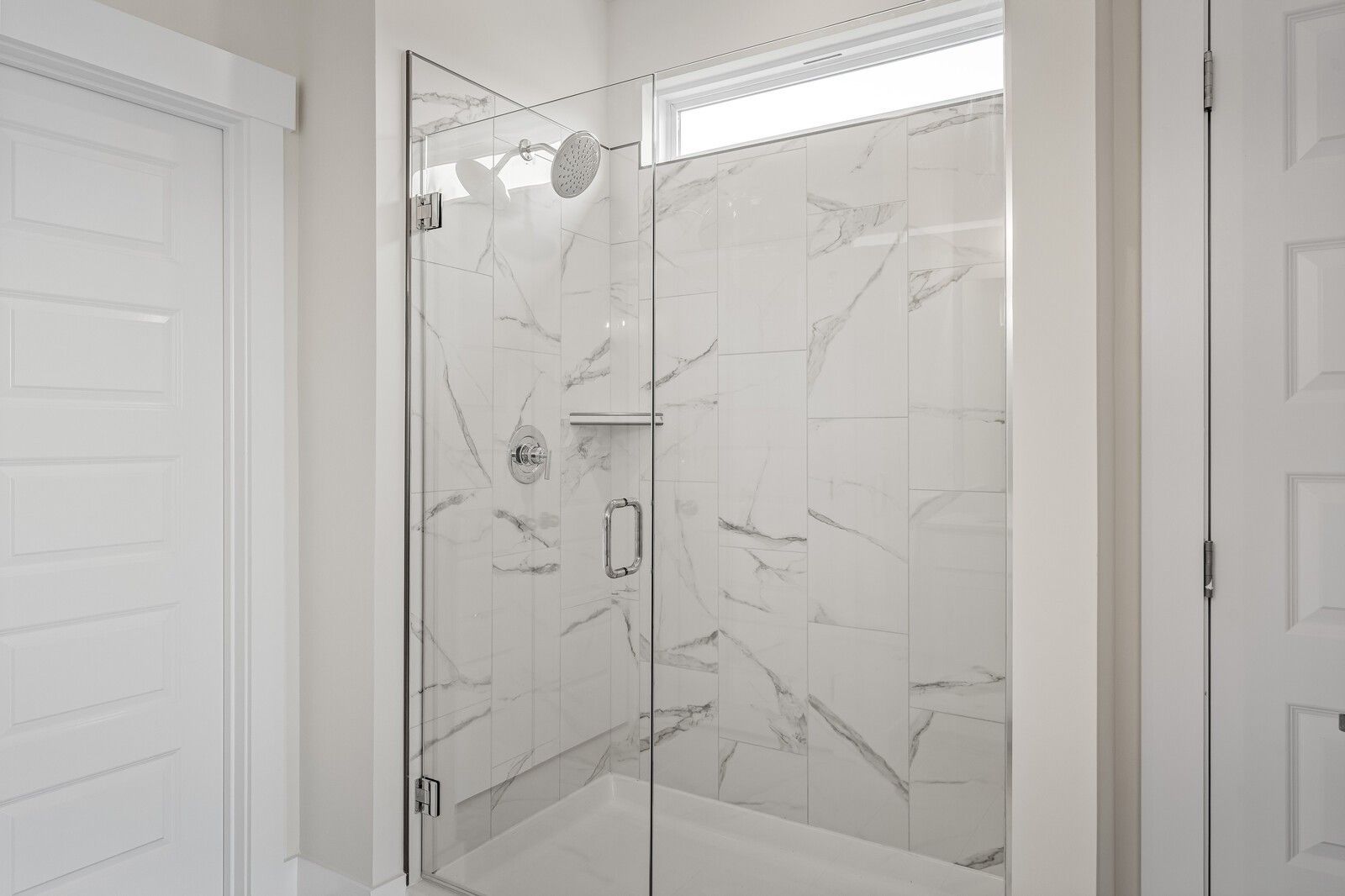 Elegant frameless glass shower with white marble tiles, rainfall head, and transom window in master bath of The Ridgeport D home, Mt. Juliet, Tennessee