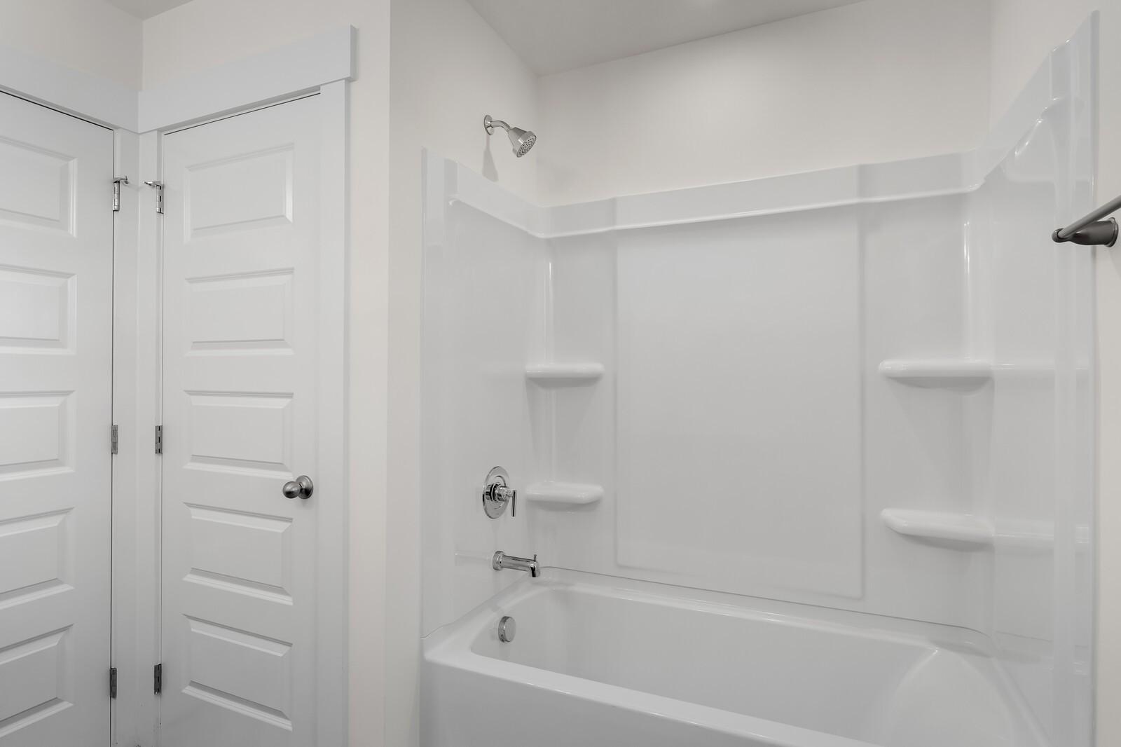 Bright white bathroom with soaking tub, glass shower enclosure, and built-in shelves in Davidson Homes The Willow C, Gallatin, Tennessee