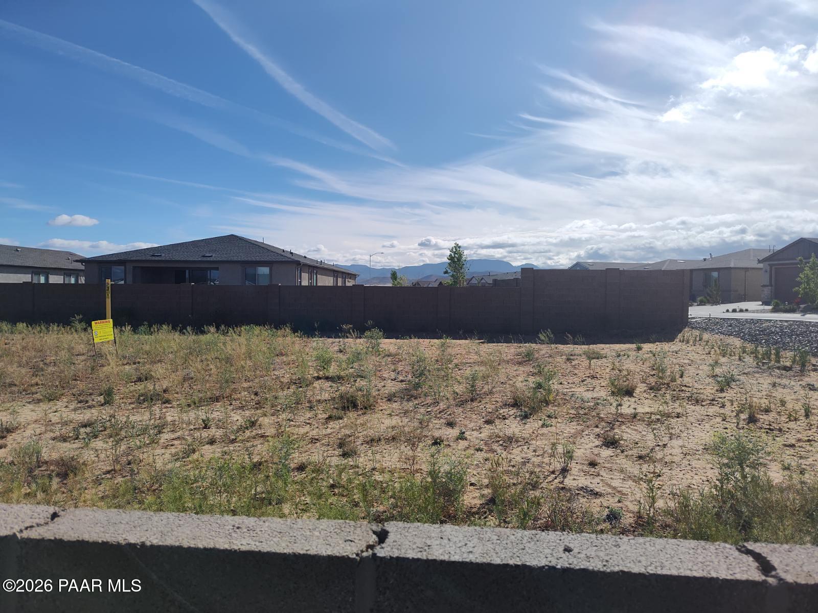 Fenced vacant lot with yellow for-sale sign, sparse desert vegetation, modern homes and mountain views in North Ridge Pronghorn Ranch, Prescott Valley AZ