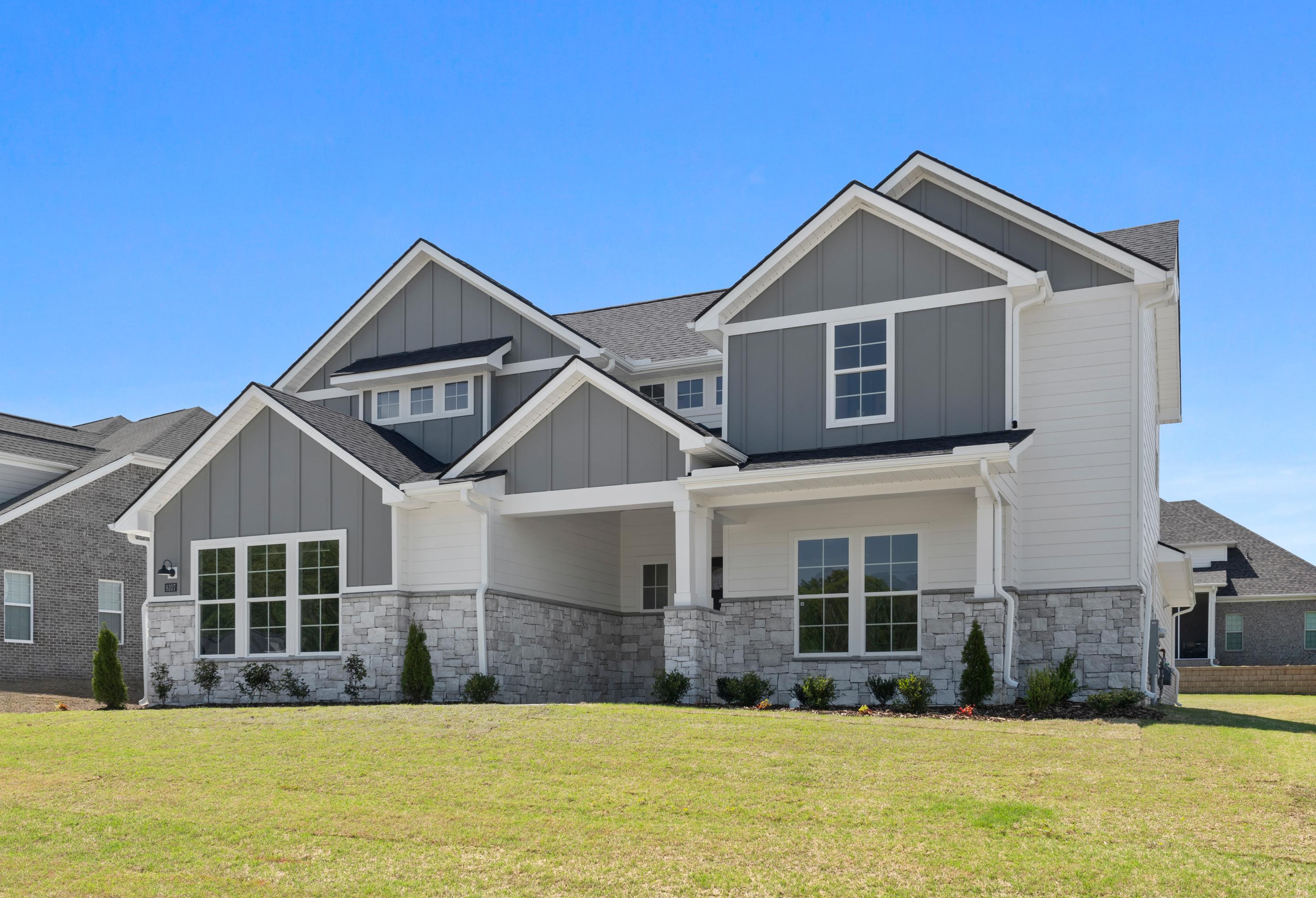 Modern front elevation of The Haven D single-story home with gray siding, stone accents, gabled roof, and covered porch on lush lawn
