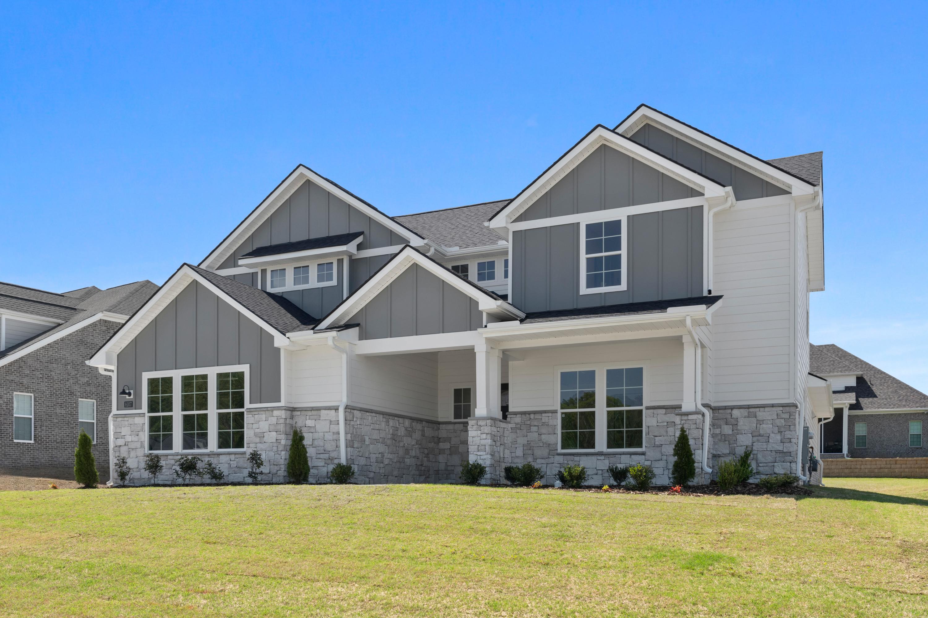 Modern front elevation of The Haven D single-story home with gray siding, stone accents, gabled roof, and covered porch on lush lawn