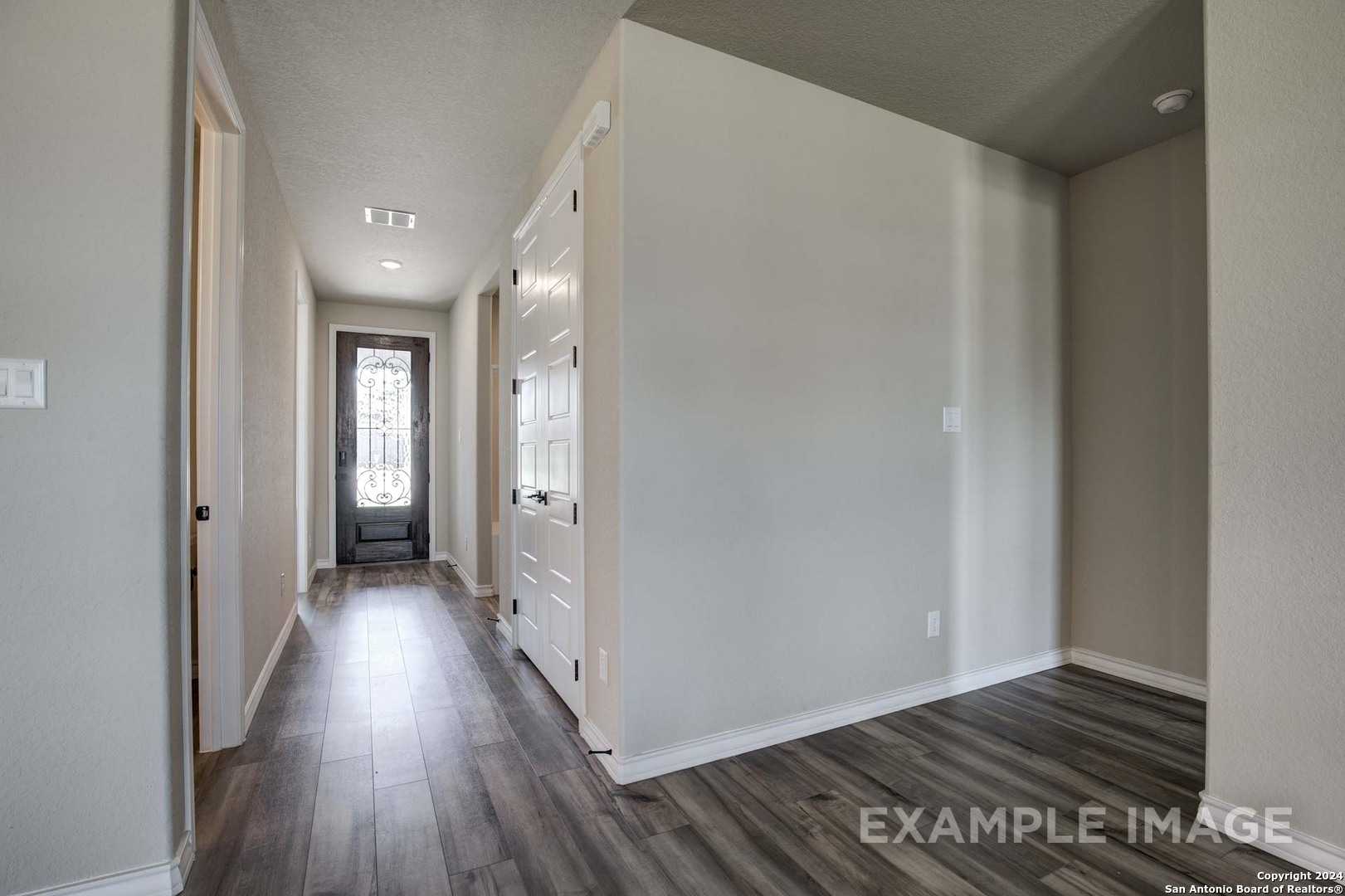 Spacious hallway with light wood laminate floors, white doors, and glass front entry in Davidson Homes The Rockford G, Ladera, San Antonio
