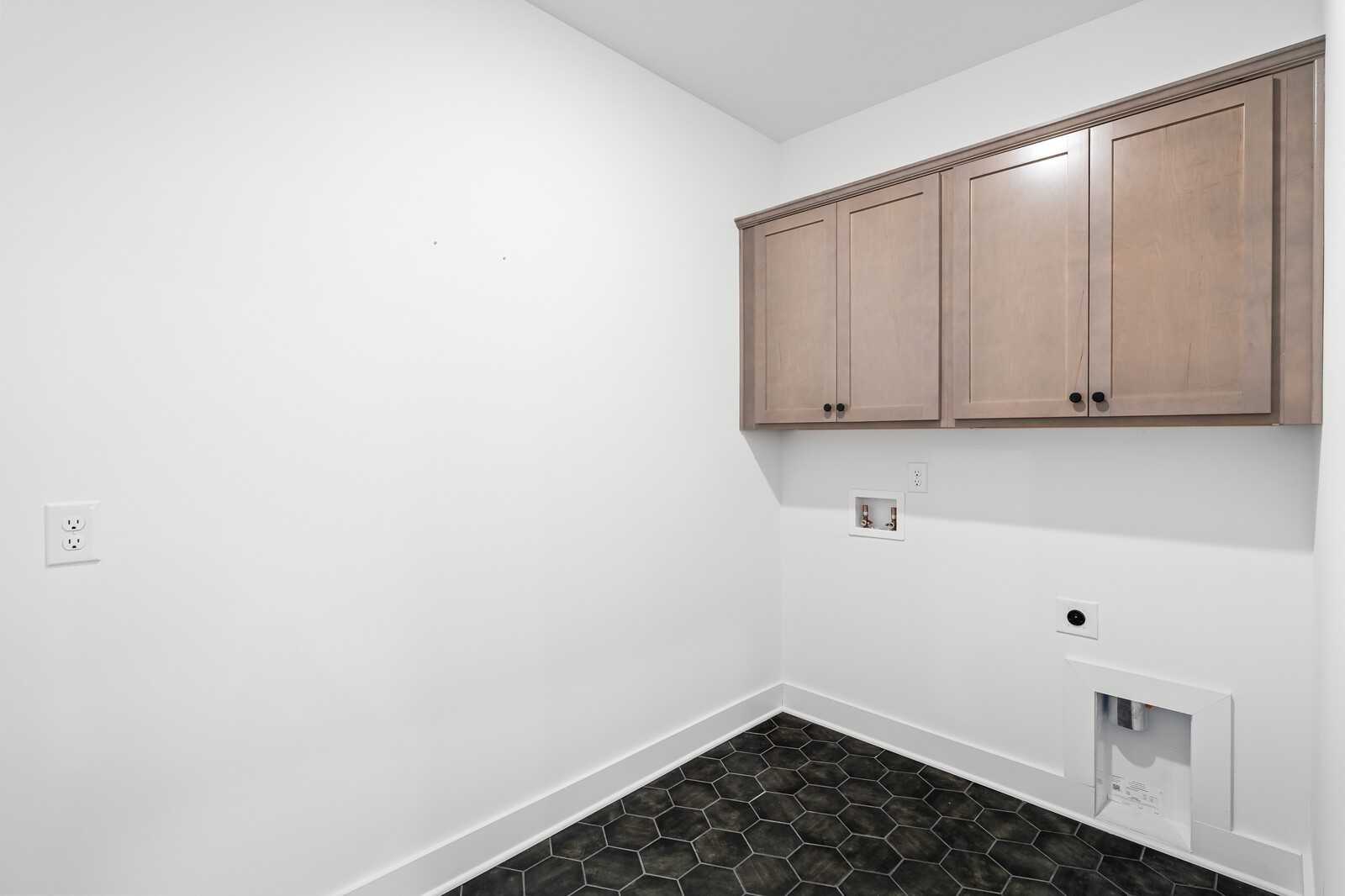 Bright laundry room with shaker upper cabinets and black hexagonal tile floor in Davidson Homes Ridgeport, Gallatin, TN