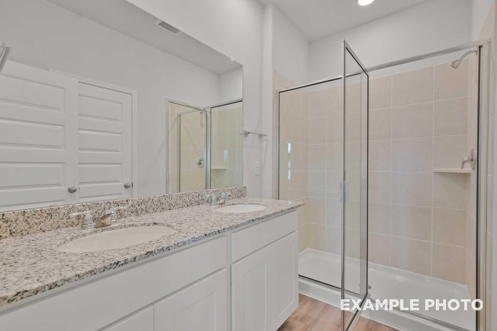 Modern master bathroom in The Comal with double granite vanity, large mirror, and glass walk-in shower