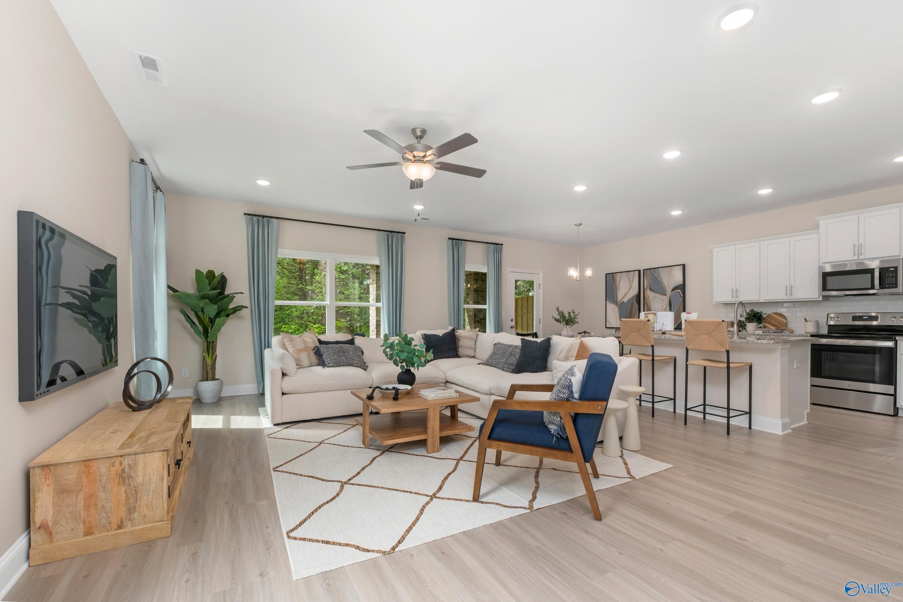 Open-concept living room with beige sectional sofa, blue armchair, ceiling fan, and adjacent kitchen bar in The Camden floor plan, Huntsville, AL