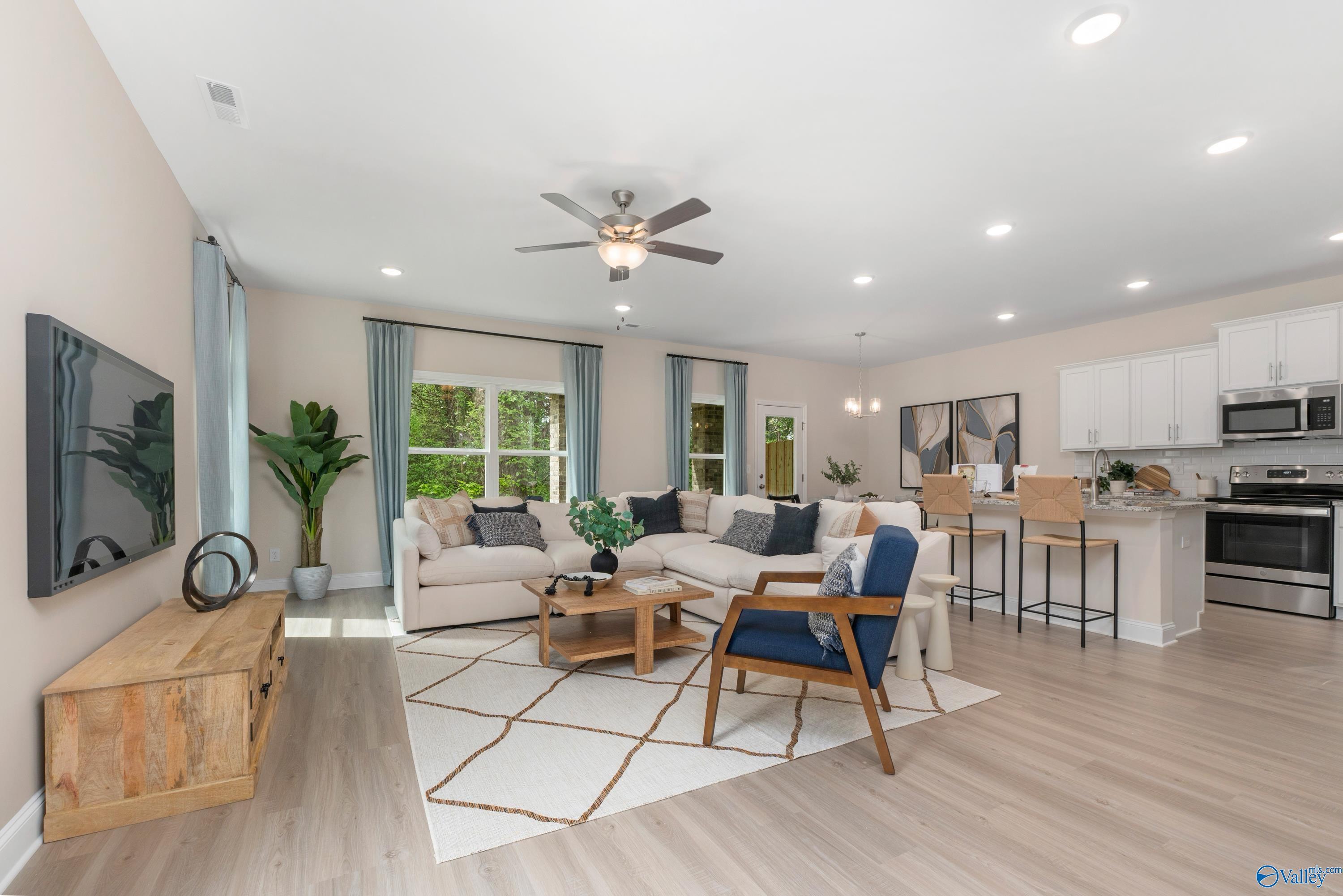 Open-concept living room with beige sectional sofa, blue armchair, ceiling fan, and adjacent kitchen bar in The Camden floor plan, Huntsville, AL