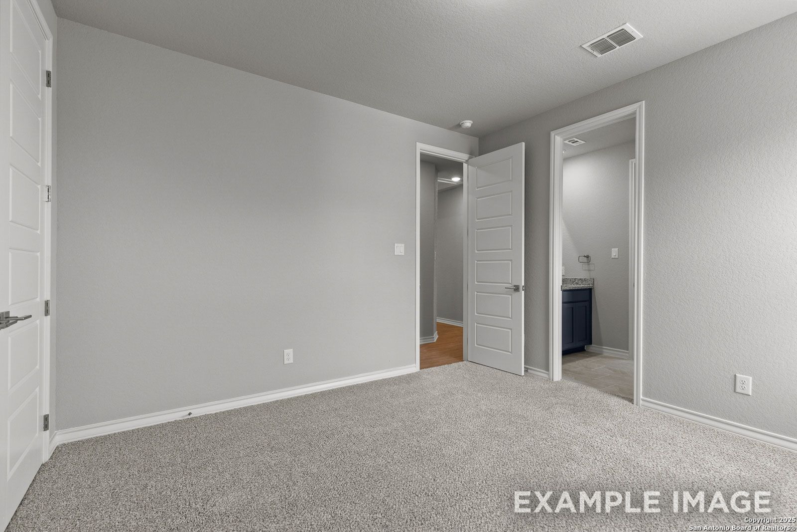 Spacious bedroom in The Oxford H floor plan featuring neutral carpet, clean wall finishes, and an attached ensuite bathroom.