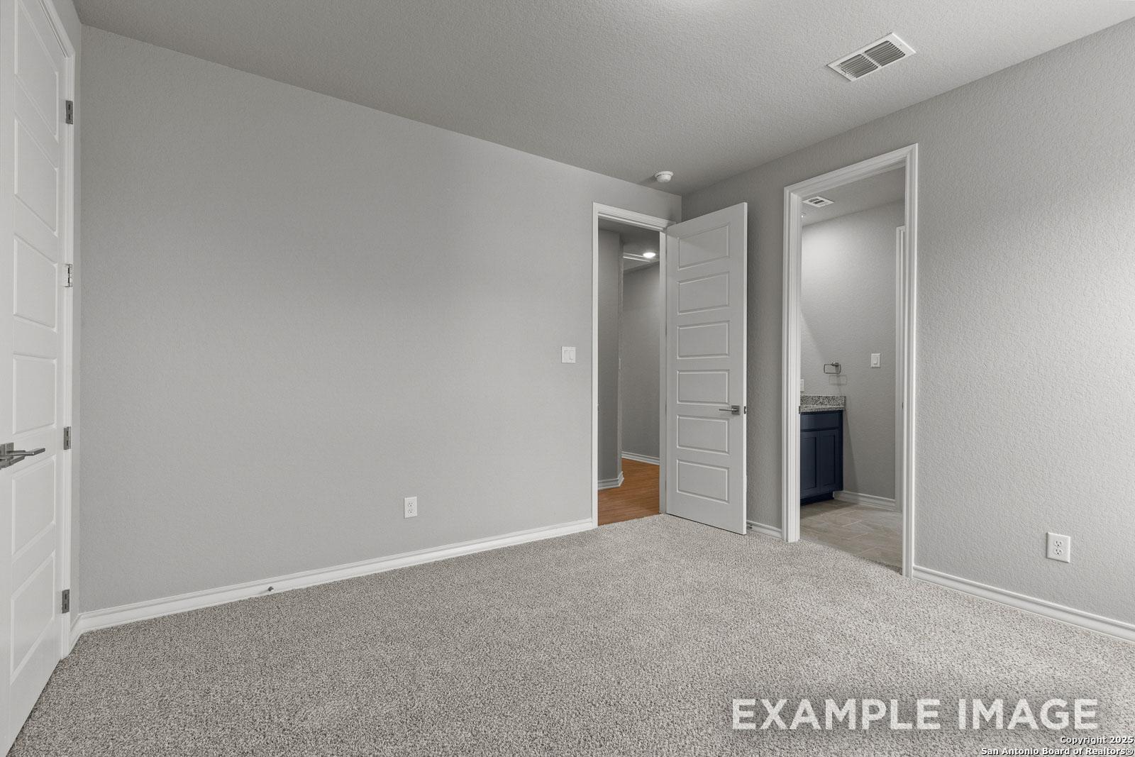Spacious bedroom in The Oxford H floor plan featuring neutral carpet, clean wall finishes, and an attached ensuite bathroom.