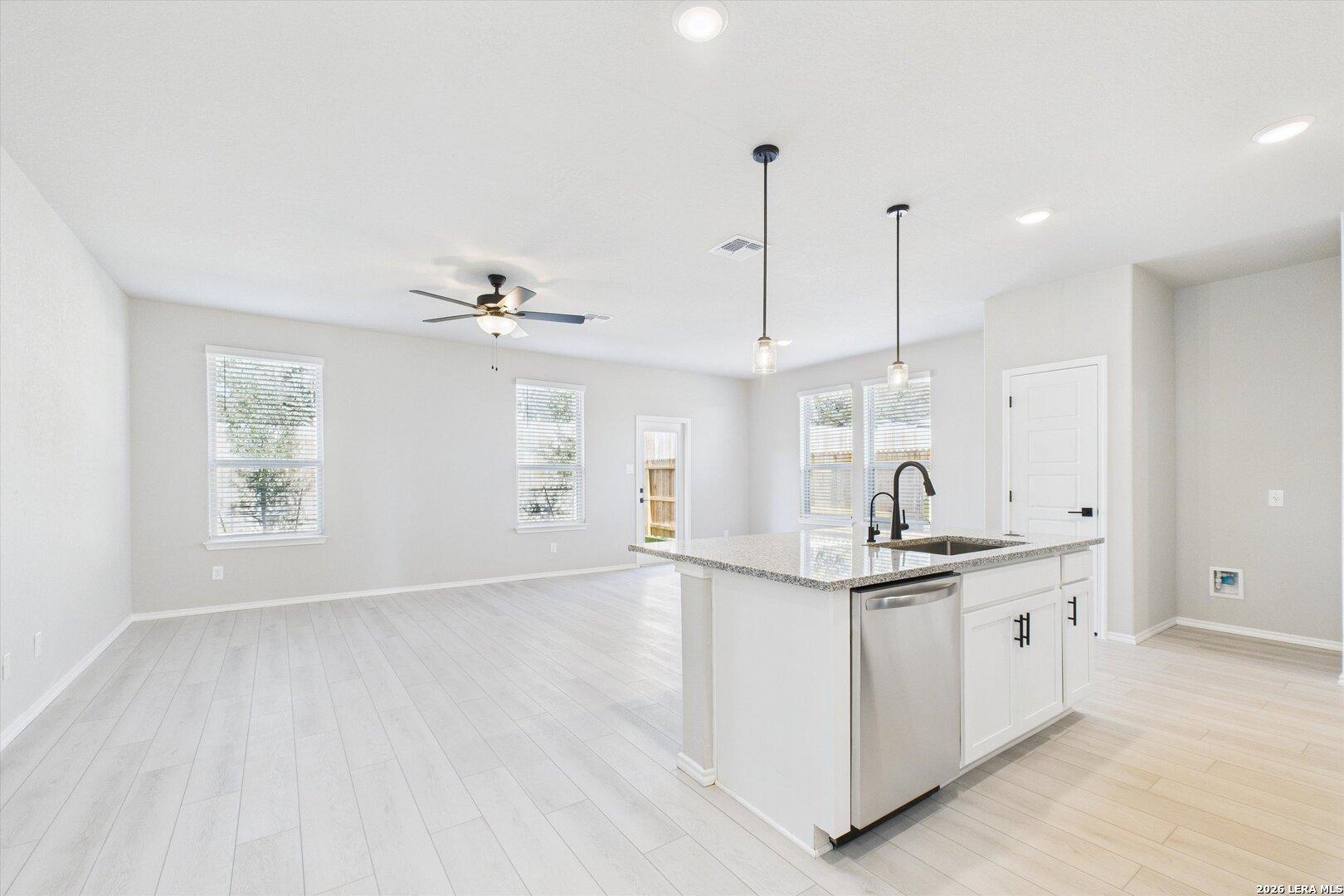 Modern open-concept kitchen with white island sink, stainless dishwasher, pendant lights, and hardwood floors in Davidson Homes The Charlotte A, San Antonio
