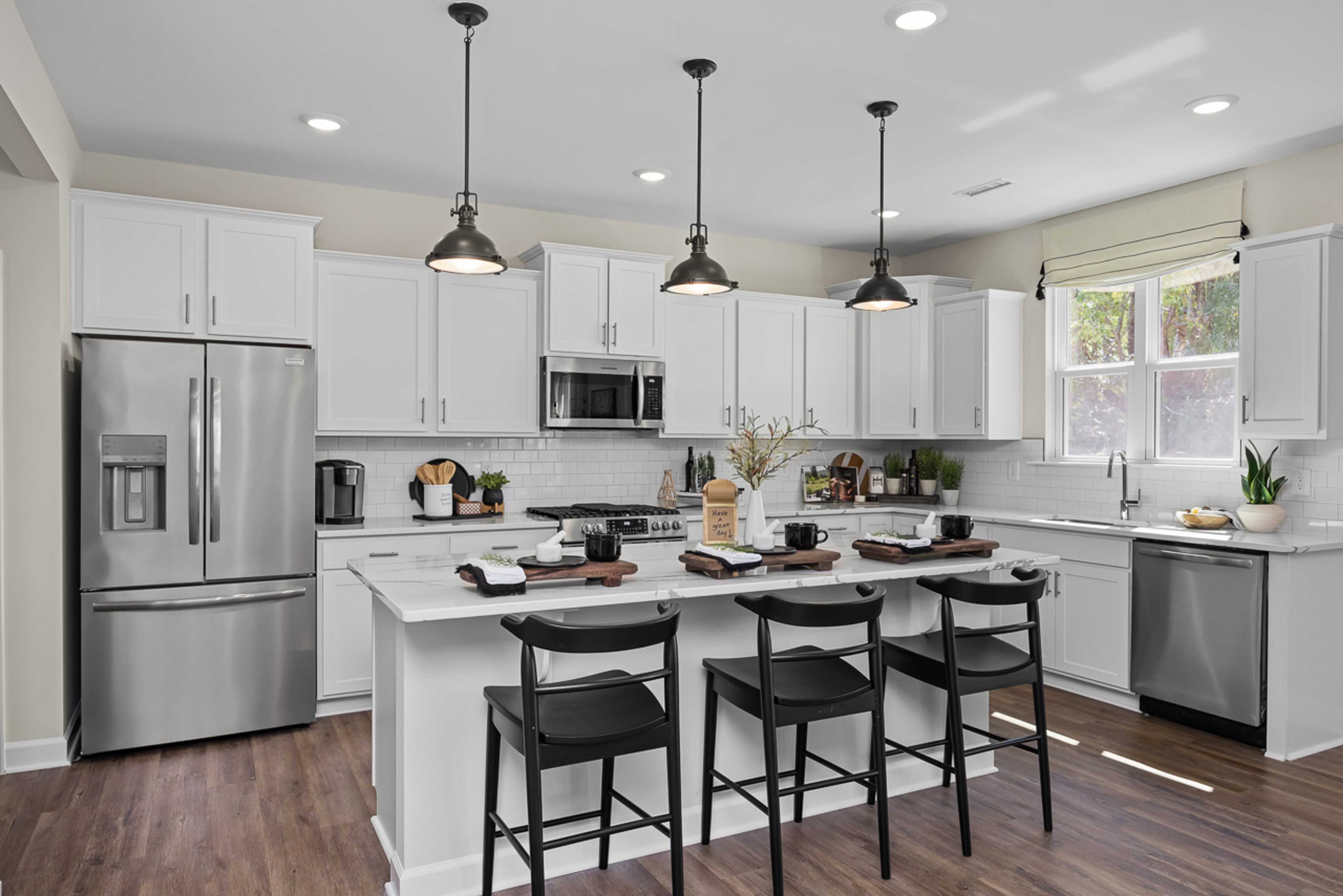 Modern kitchen in Wellers Knoll Lillington NC with white cabinets, stainless steel appliances, island bar, black stools, hardwood floors