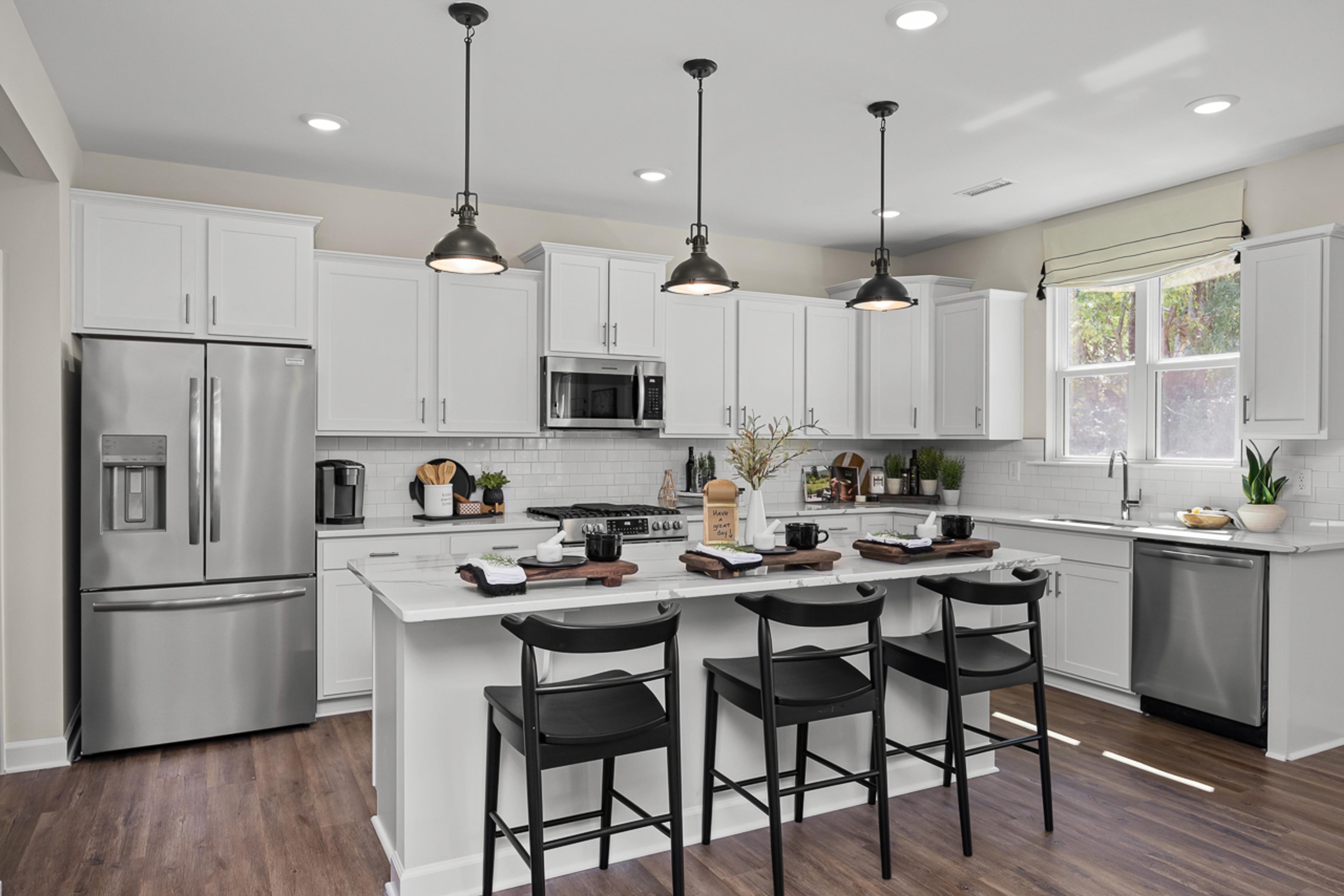 Modern kitchen in Wellers Knoll Lillington NC with white cabinets, stainless steel appliances, island bar, black stools, hardwood floors